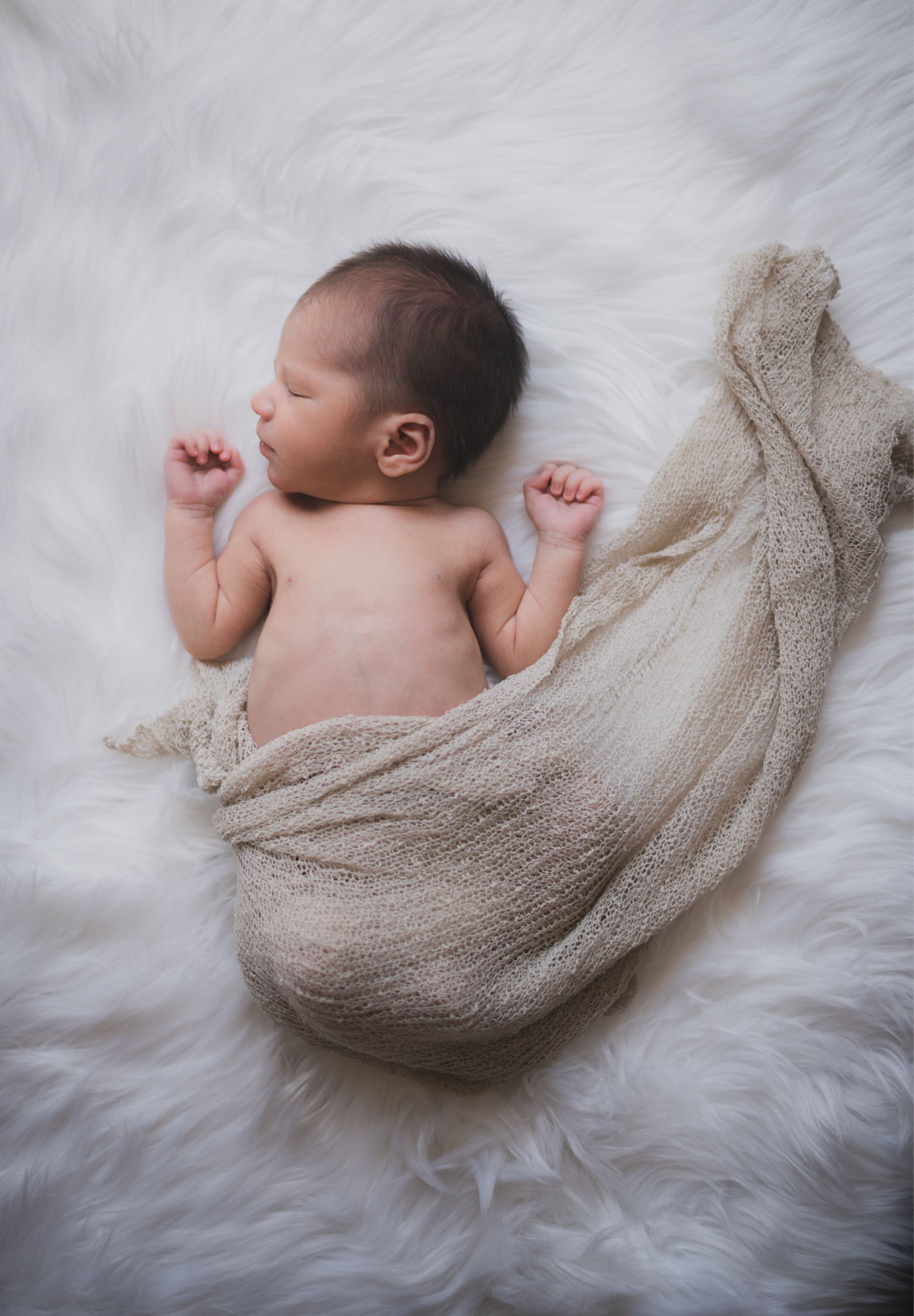 Dark and moody portrait of a newborn baby boy in the arms of his mother in their home in Hesperia California. Mother and baby both look happy as they pose in a lifestyle photoshoot for the inland empires number one family photographer. Baby boy is asian with fuzzy black hair in a child’s lifestyle photo shoot with a female photographer in high desert