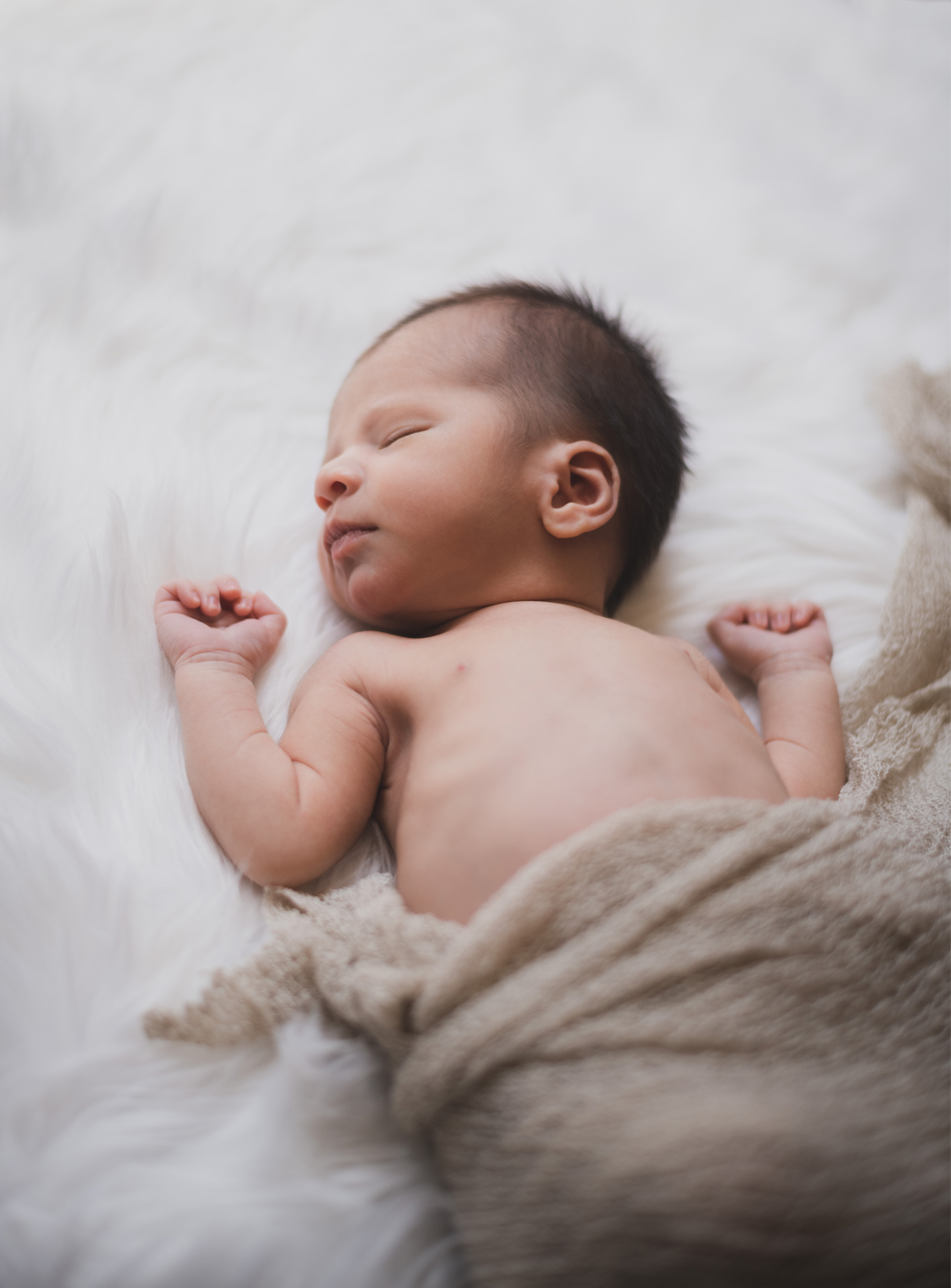 Dark and moody portrait of a newborn baby boy in the arms of his mother in their home in Hesperia California. Mother and baby both look happy as they pose in a lifestyle photoshoot for the inland empires number one family photographer. Baby boy is asian with fuzzy black hair in a child’s lifestyle photo shoot with a female photographer in high desert