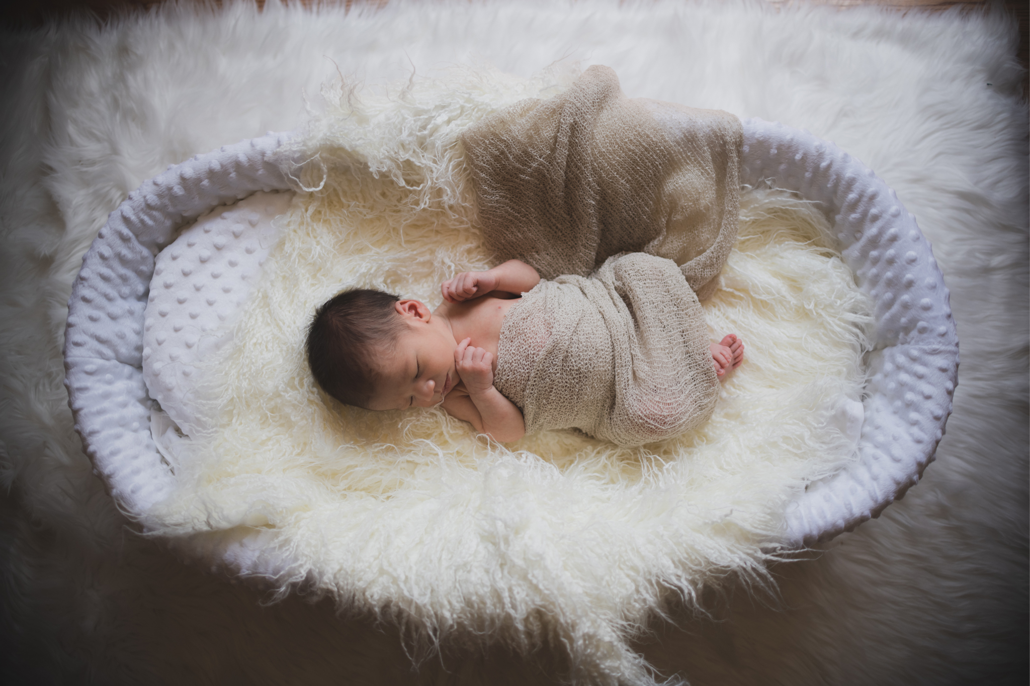 Dark and moody portrait of a newborn baby boy in the arms of his mother in their home in Hesperia California. Mother and baby both look happy as they pose in a lifestyle photoshoot for the inland empires number one family photographer. Baby boy is asian with fuzzy black hair in a child’s lifestyle photo shoot with a female photographer in high desert