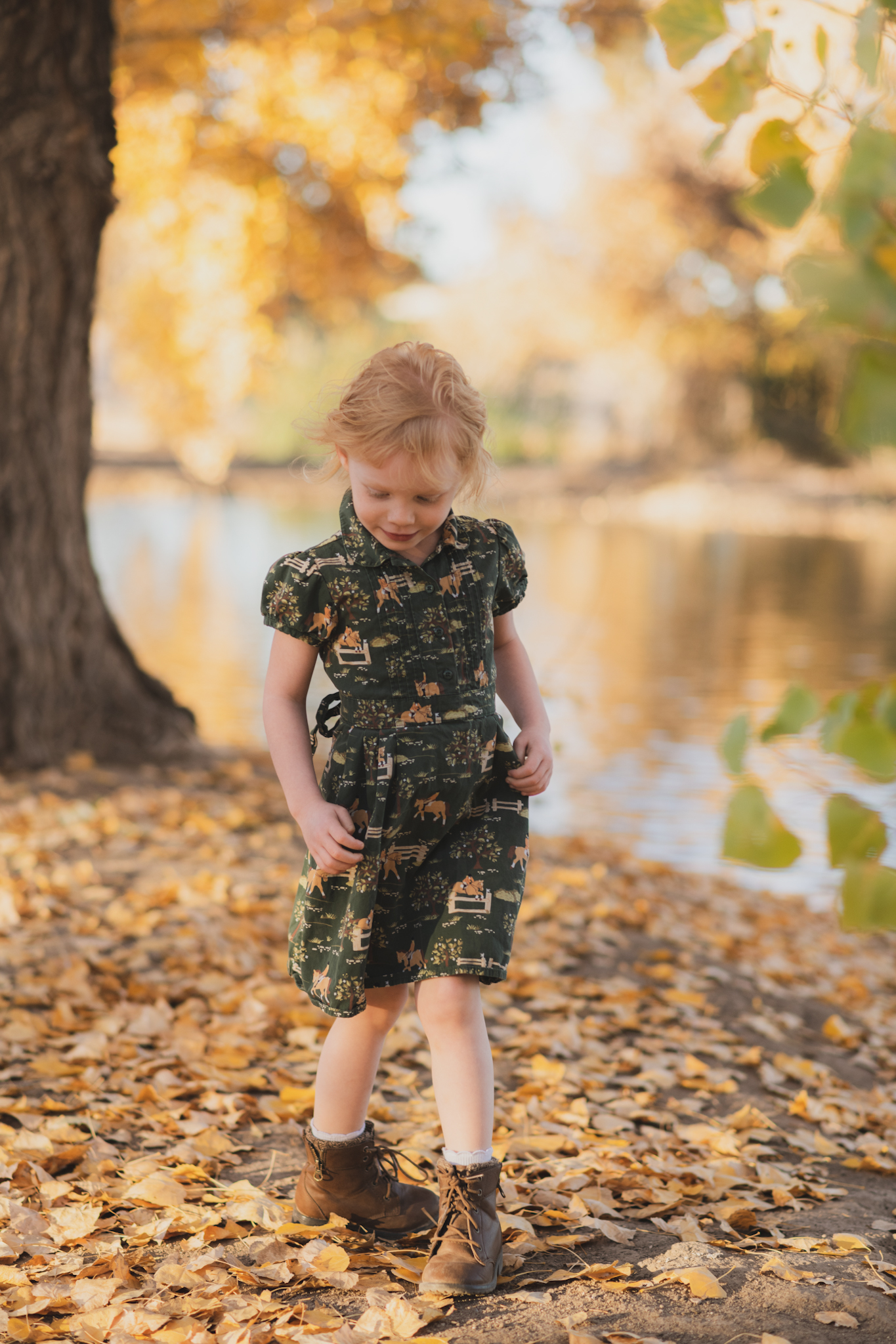 Dark and moody photo shoot of a four year old girl in a pink cowgirl dress at the Hesperia Lakes recreational park in Hesperia California. She is smiling and spinning for the inland empires best childr photographer. Big trees with lots of orange leaves are the backdrop of the lifestyle photoshoot in the high desert