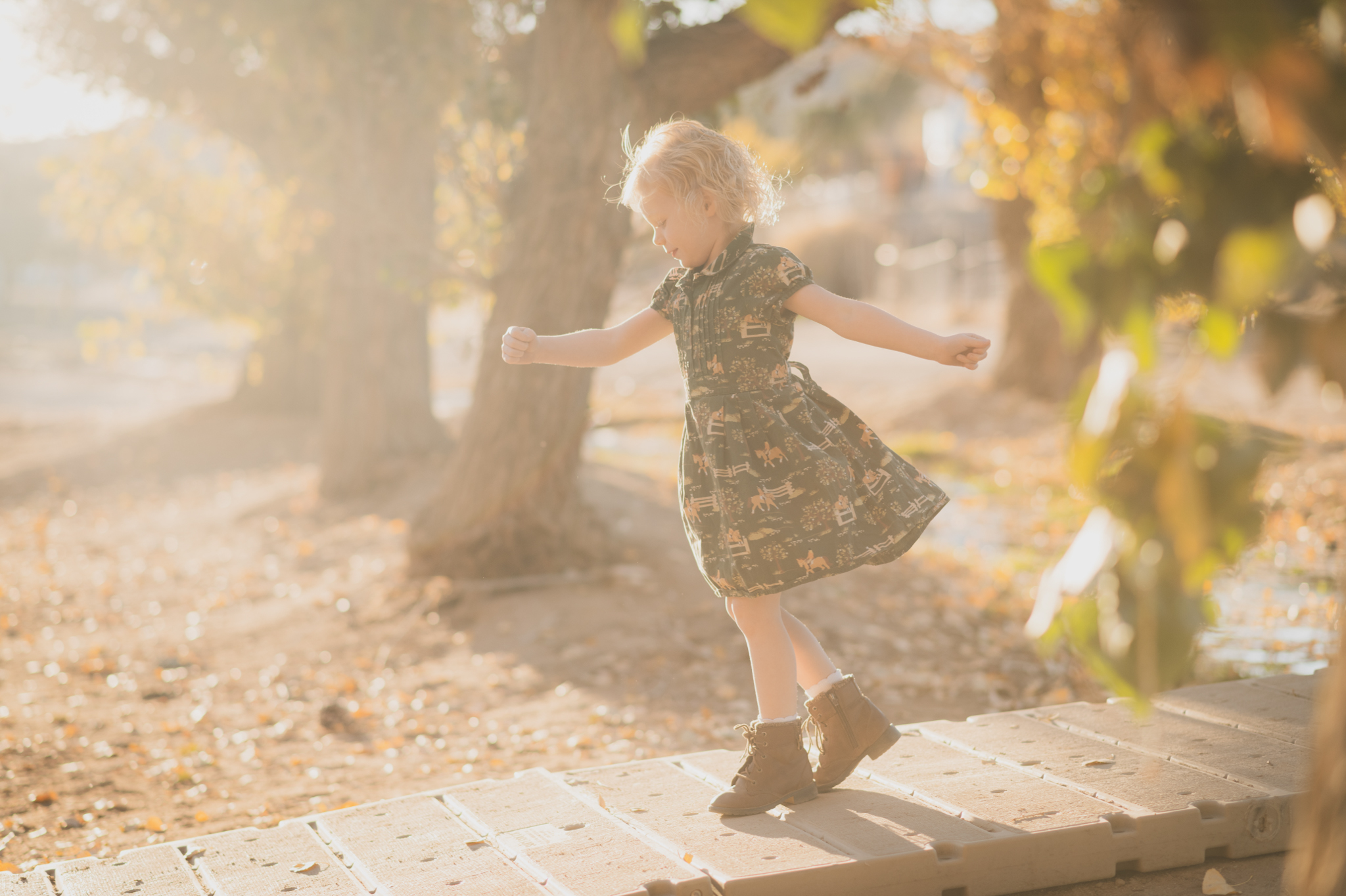 Dark and moody photo shoot of a four year old girl in a pink cowgirl dress at the Hesperia Lakes recreational park in Hesperia California. She is smiling and spinning for the inland empires best childr photographer. Big trees with lots of orange leaves are the backdrop of the lifestyle photoshoot in the high desert