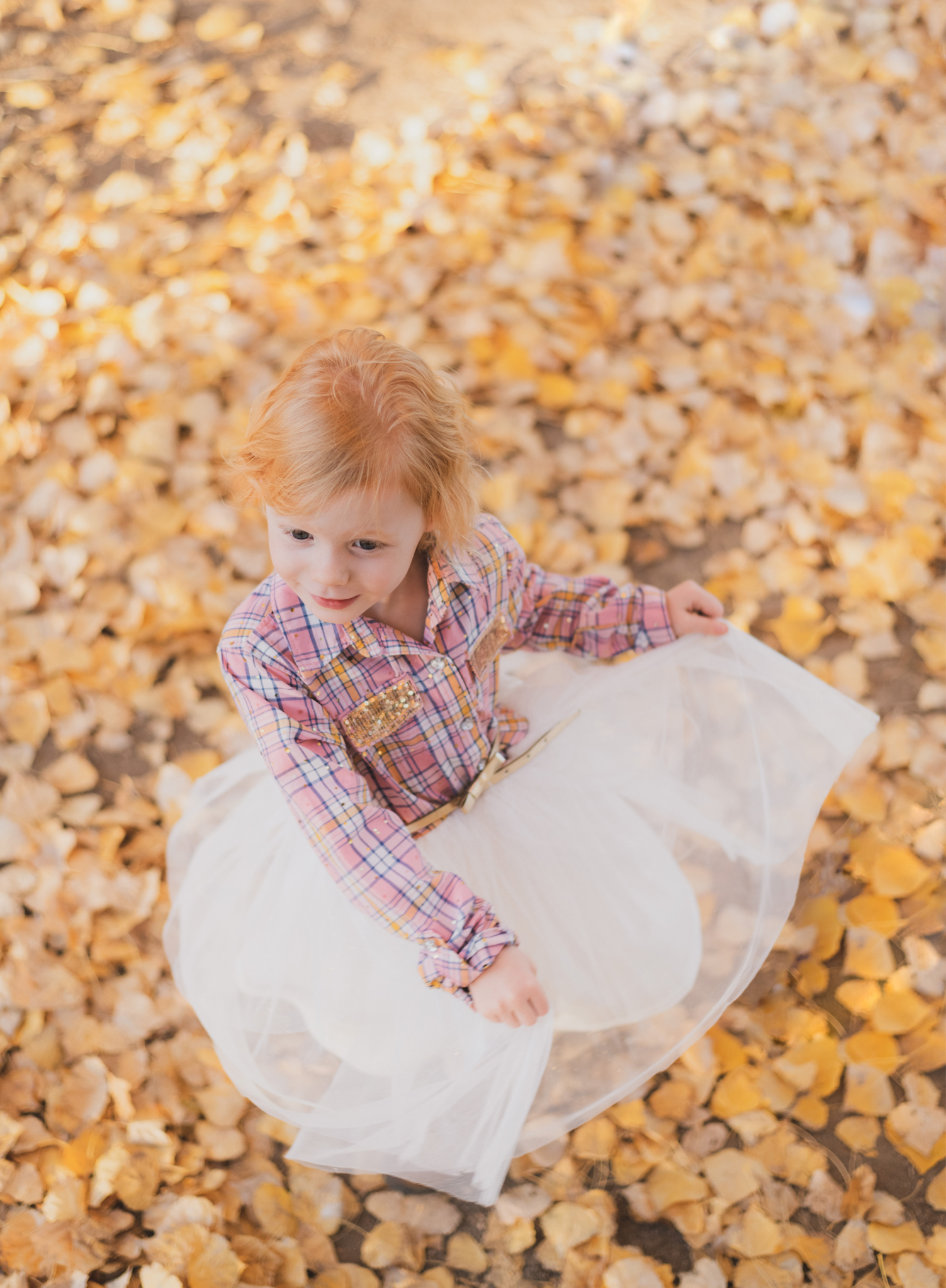 Dark and moody photo shoot of a four year old girl in a pink cowgirl dress at the Hesperia Lakes recreational park in Hesperia California. She is smiling and spinning for the inland empires best childr photographer. Big trees with lots of orange leaves are the backdrop of the lifestyle photoshoot in the high desert