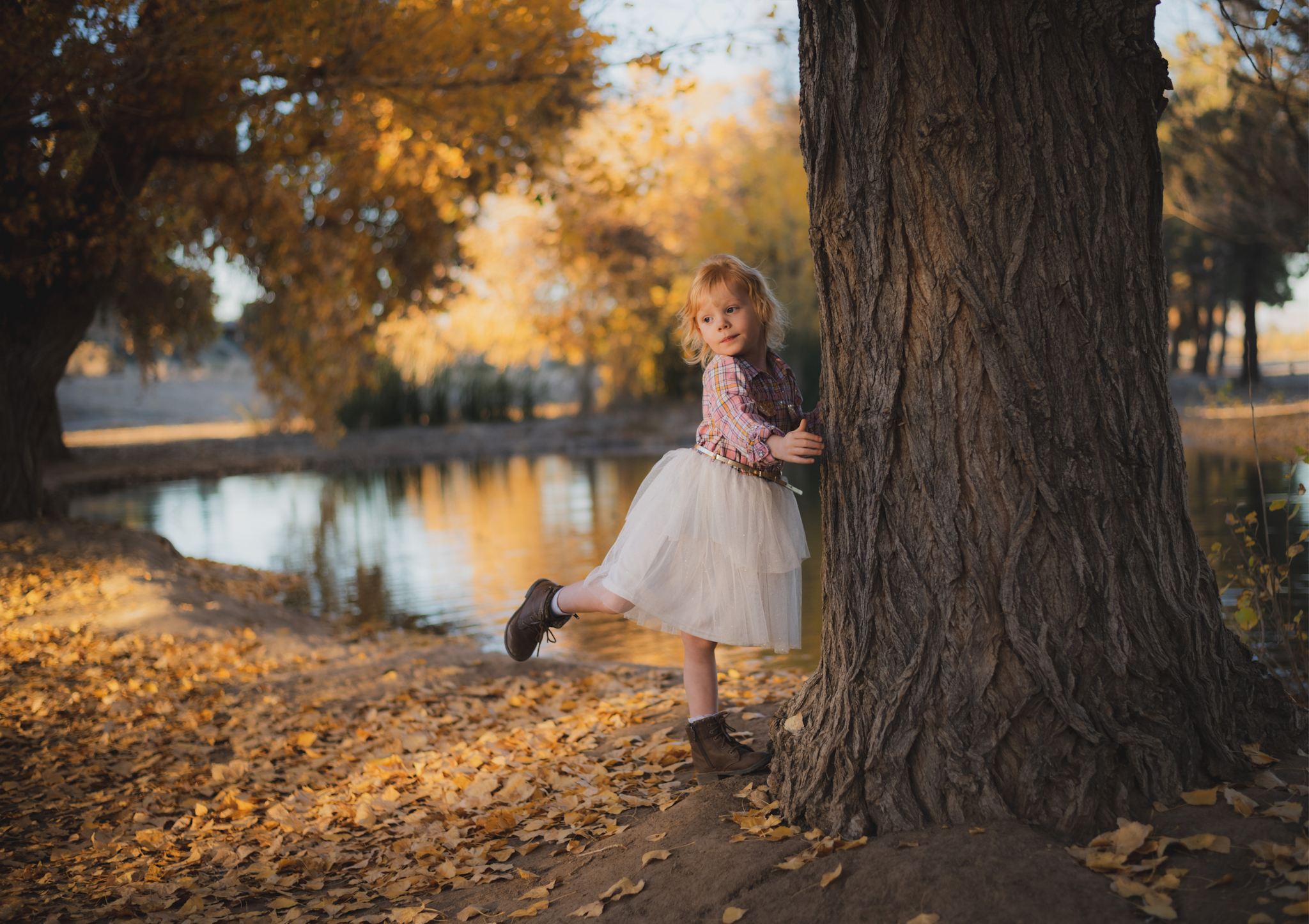 Dark and moody photo shoot of a four year old girl in a pink cowgirl dress at the Hesperia Lakes recreational park in Hesperia California. She is smiling and spinning for the inland empires best childr photographer. Big trees with lots of orange leaves are the backdrop of the lifestyle photoshoot in the high desert