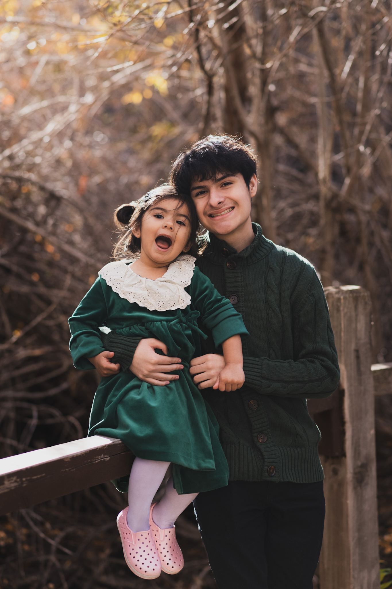 dark and moody portraits of a family in the forest mountains of Wrightwood california. The family is dressed in formal clothes and posing for the camera of the high deserts #1 best family photographer. The mother and daughter are wearing matching green velvet dresses and smiling. The father and son are wearing green sweatshirts. The San Bernardino mountain trees are the backdrop of this family photoshoot in the inland empire