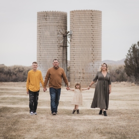 Light and airy portrait of a family posing for the high deserts best photographer at the Mojave narrows national park in Victorville California. They are dressed in formal clothing in front of giant water towers and smiling for the camera.
