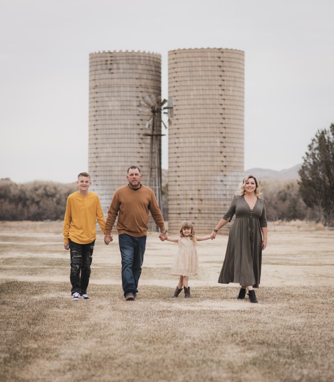Light and airy portrait of a family posing for the high deserts best photographer at the Mojave narrows national park in Victorville California. They are dressed in formal clothing in front of giant water towers and smiling for the camera.