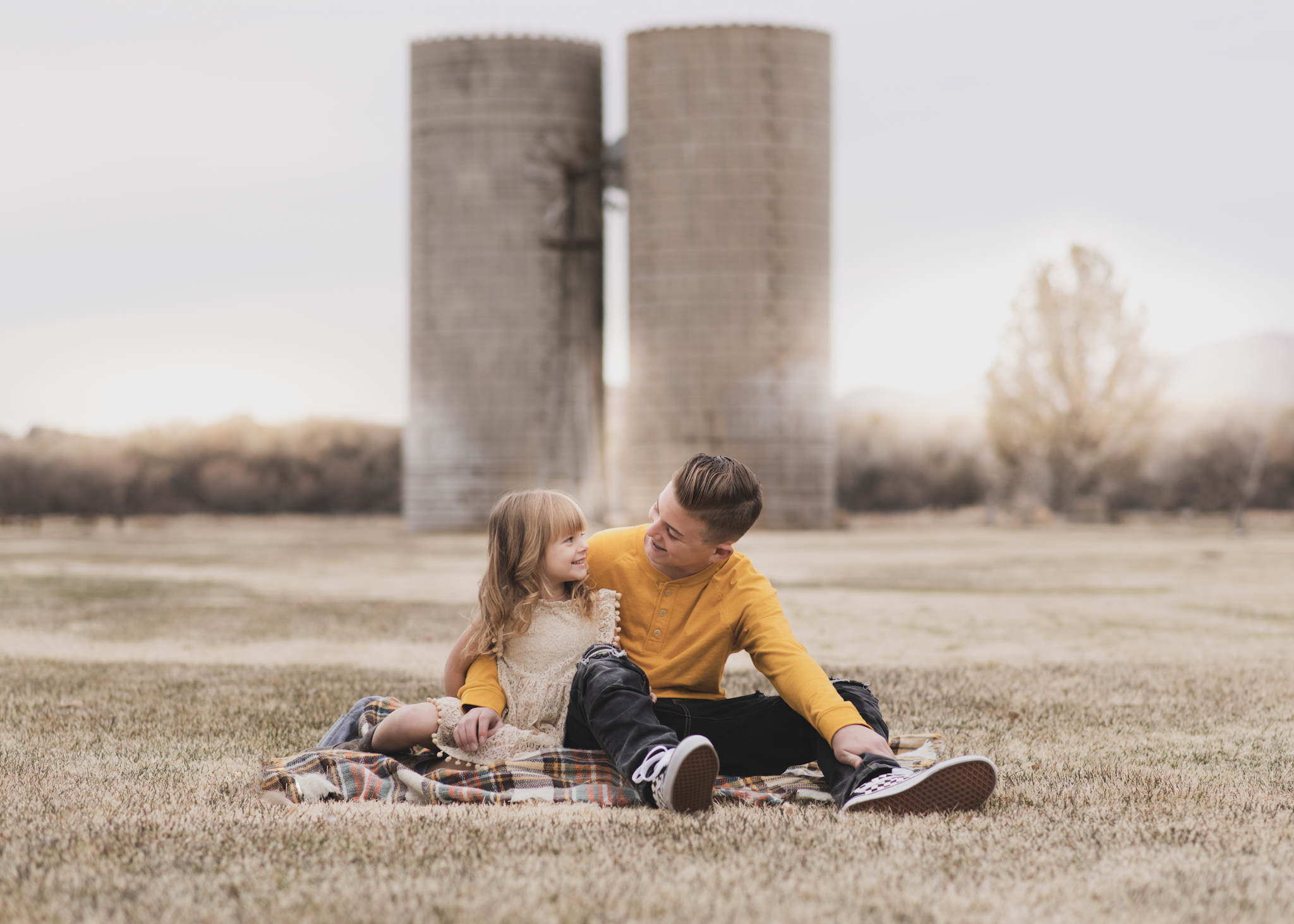 Light and airy portrait of a family posing for the high deserts best photographer at the Mojave narrows national park in Victorville California. They are dressed in formal clothing in front of giant water towers and smiling for the camera