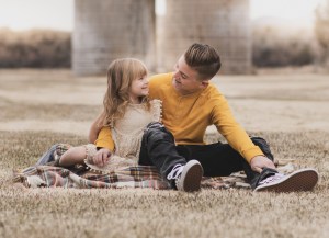 Light and airy portrait of a family posing for the high deserts best photographer at the Mojave narrows national park in Victorville California. They are dressed in formal clothing in front of giant water towers and smiling for the camera