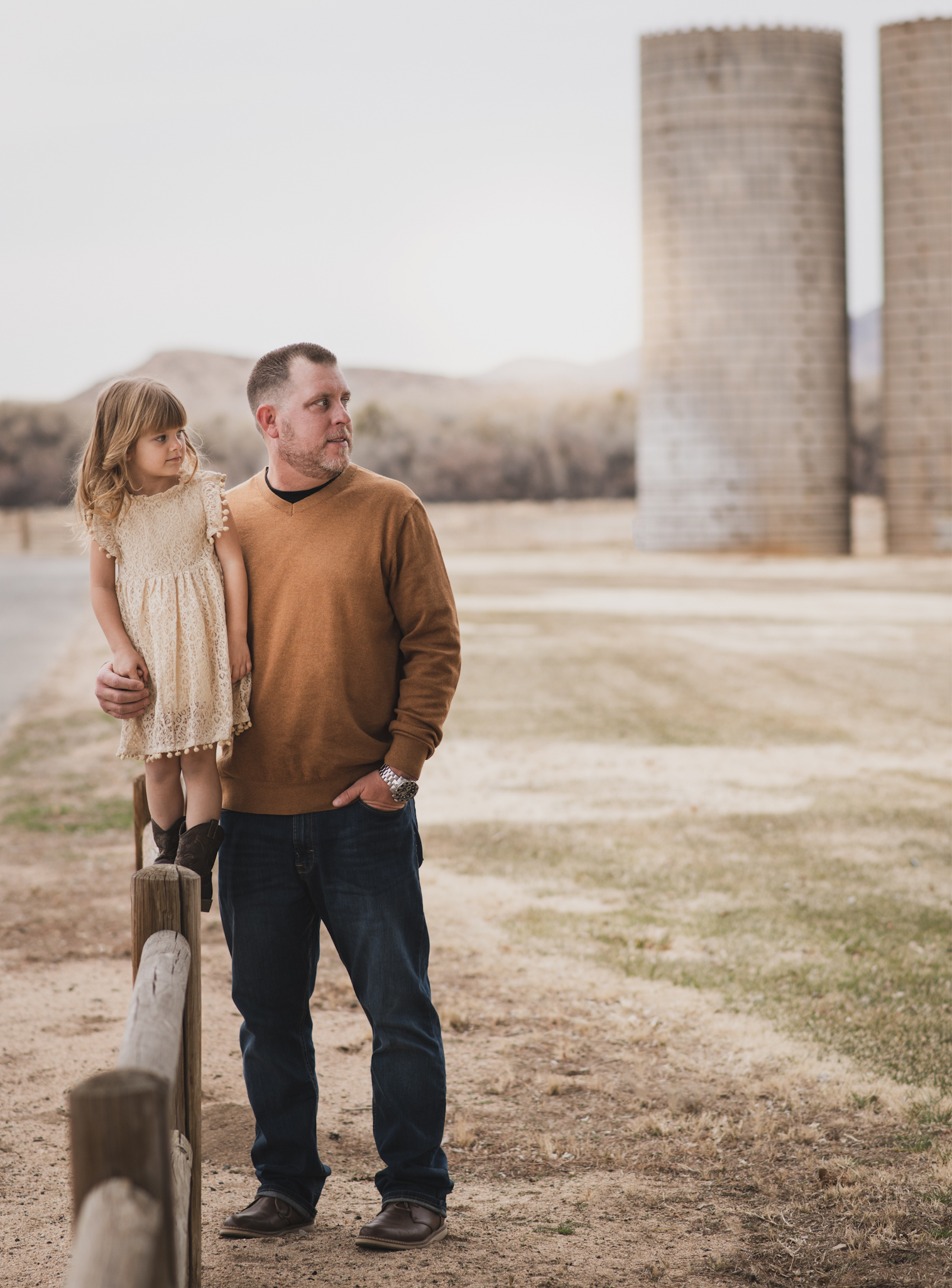 Light and airy portrait of a family posing for the high deserts best photographer at the Mojave narrows national park in Victorville California. They are dressed in formal clothing in front of giant water towers and smiling for the camera