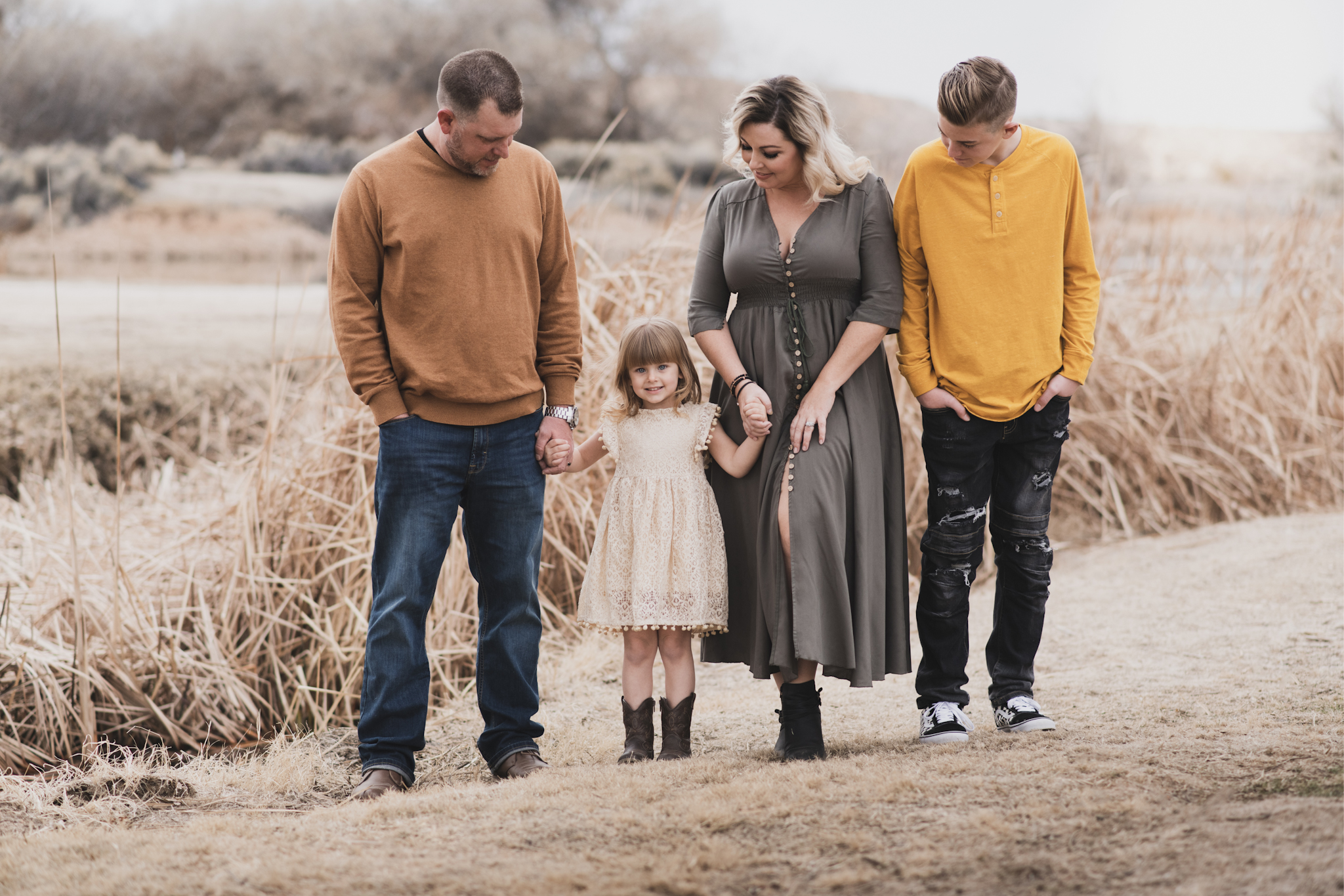 Light and airy portrait of a family posing for the high deserts best photographer at the Mojave narrows national park in Victorville California. They are dressed in formal clothing in front of giant water towers and smiling for the camera