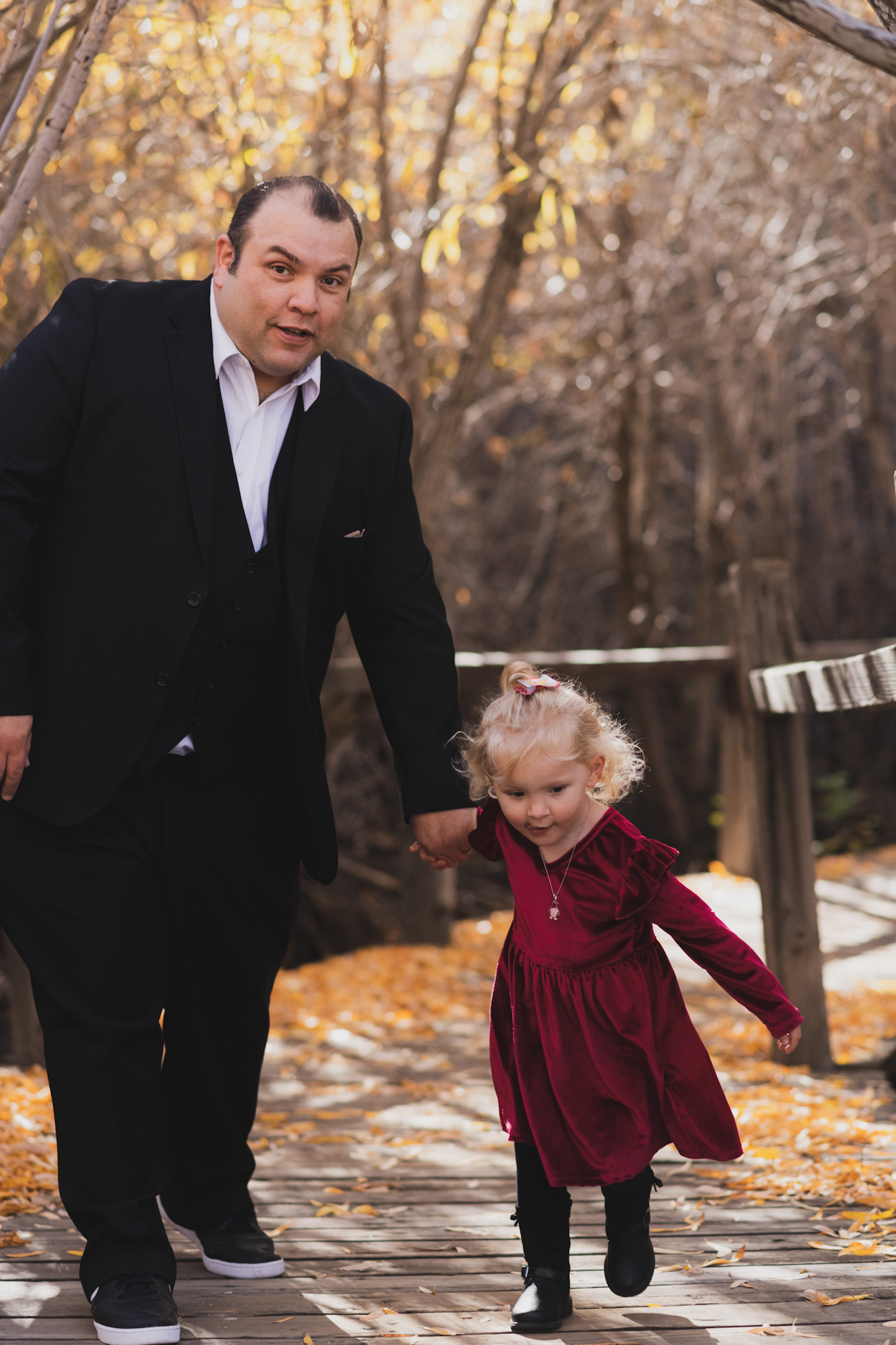 dark and moody portraits of a family in the forest mountains of Wrightwood california. The family is dressed in formal clothes and posing for the camera of the high deserts #1 best family photographer. The mother and daughter are wearing matching red velvet dresses and smiling. The father and baby son are wearing black tuxedos and bow ties. The San Bernardino mountain trees are the backdrop of this family photoshoot in the inland empire