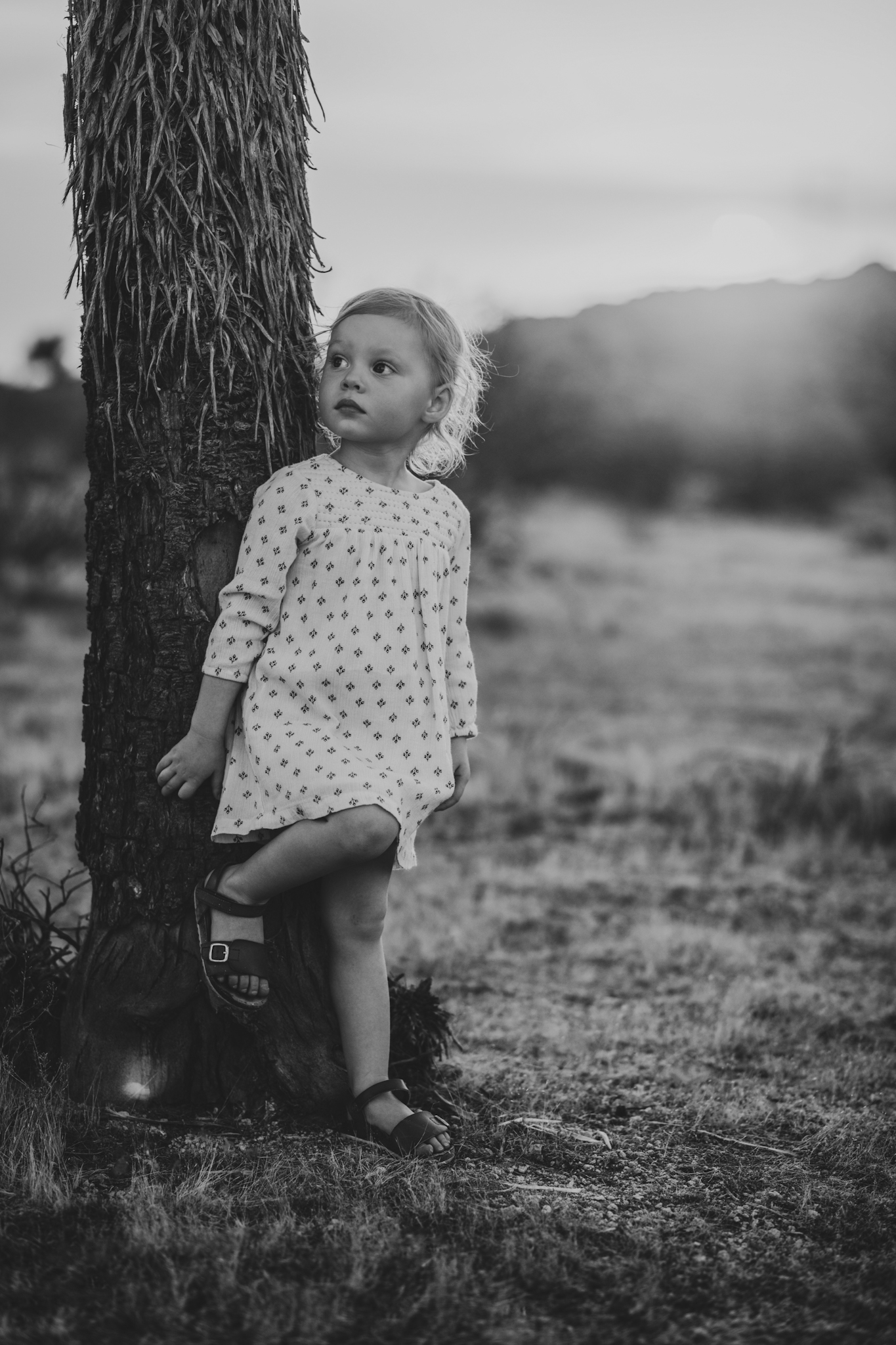 Dark and moody family portraits taken at sunset in the beautiful california mountains in lucerne valley. The high desert sky is behind the mother and father who are wearing red. The three year old daughter is smiling at the high deserts best family photographer