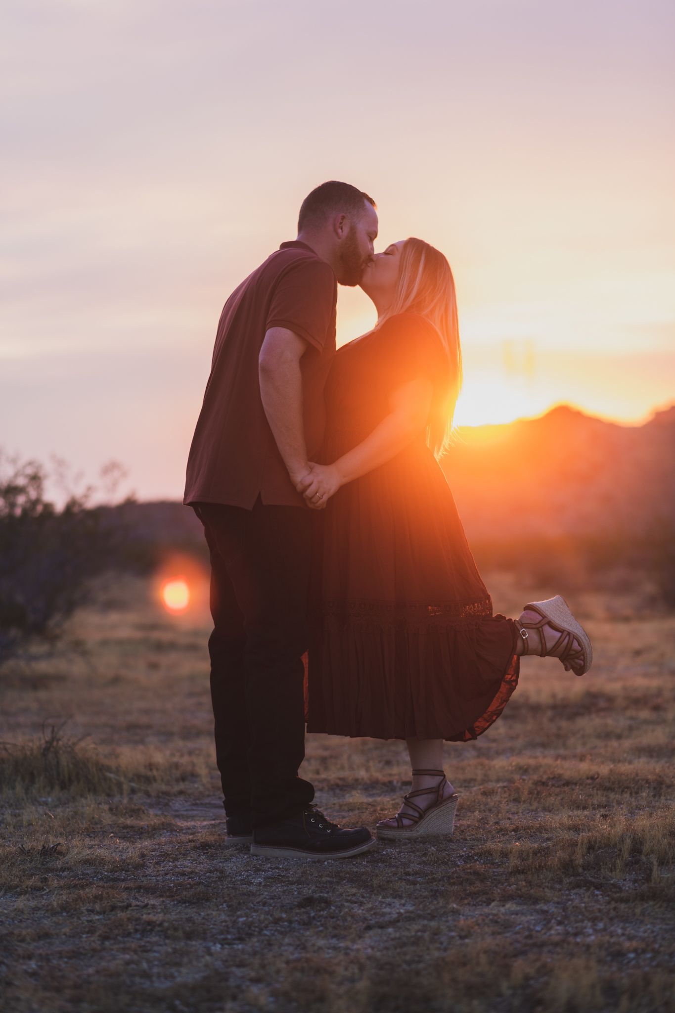 Dark and moody family portraits taken at sunset in the beautiful california mountains in lucerne valley. The high desert sky is behind the mother and father who are wearing red. The three year old daughter is smiling at the high deserts best family photographer