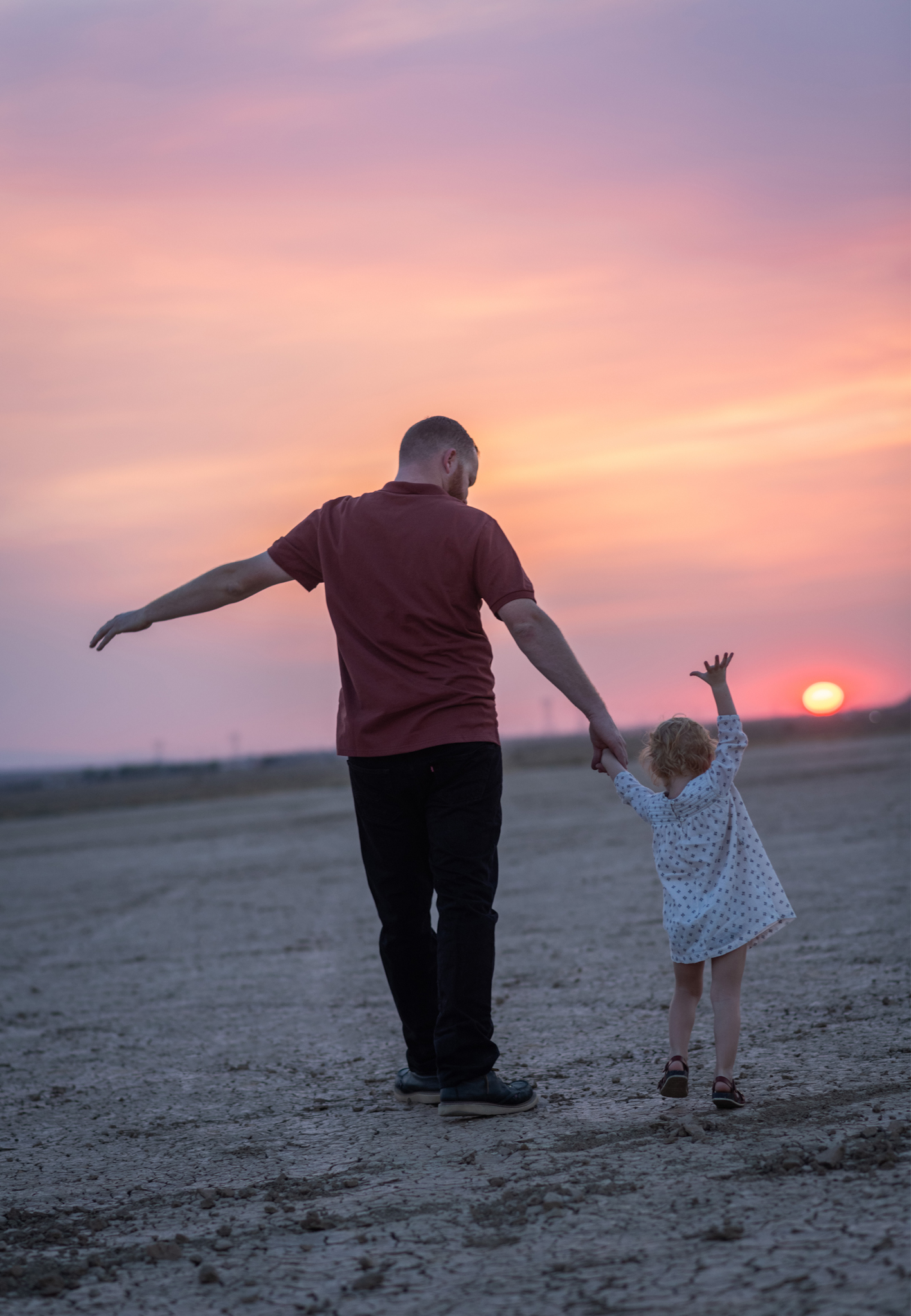 Dark and moody family portraits taken at sunset in the beautiful california mountains in lucerne valley. The high desert sky is behind the mother and father who are wearing red. The three year old daughter is smiling at the high deserts best family photographer