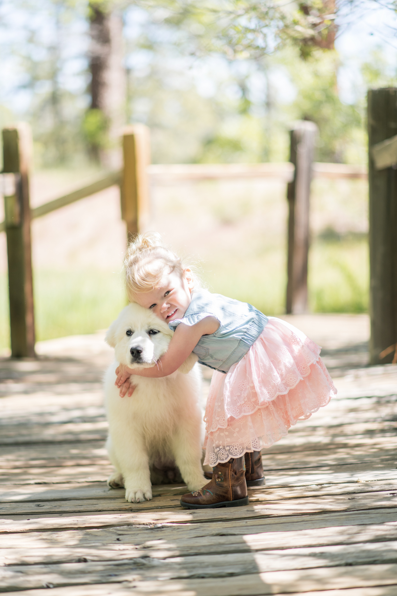 Light and airy photo shoot of a little blonde girl and her poodle puppy posing for the high deserts best photographer in the forest of Wrightwood California. She is wearing a cute dress and walking on a bridge in the inland empire