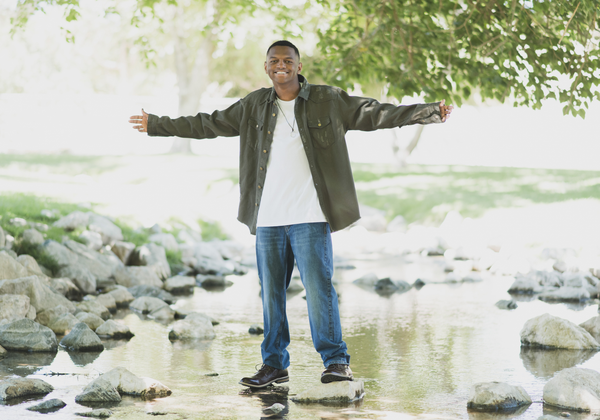 Light and airy family photoshoot at Hesperia Lake Park in the Inland empire. A Large family smiles and laughs for the high deserts best photographer. The scenery is green with lots of beautiful trees and nature. There is a pond in the background of these family portraits in the inland empire