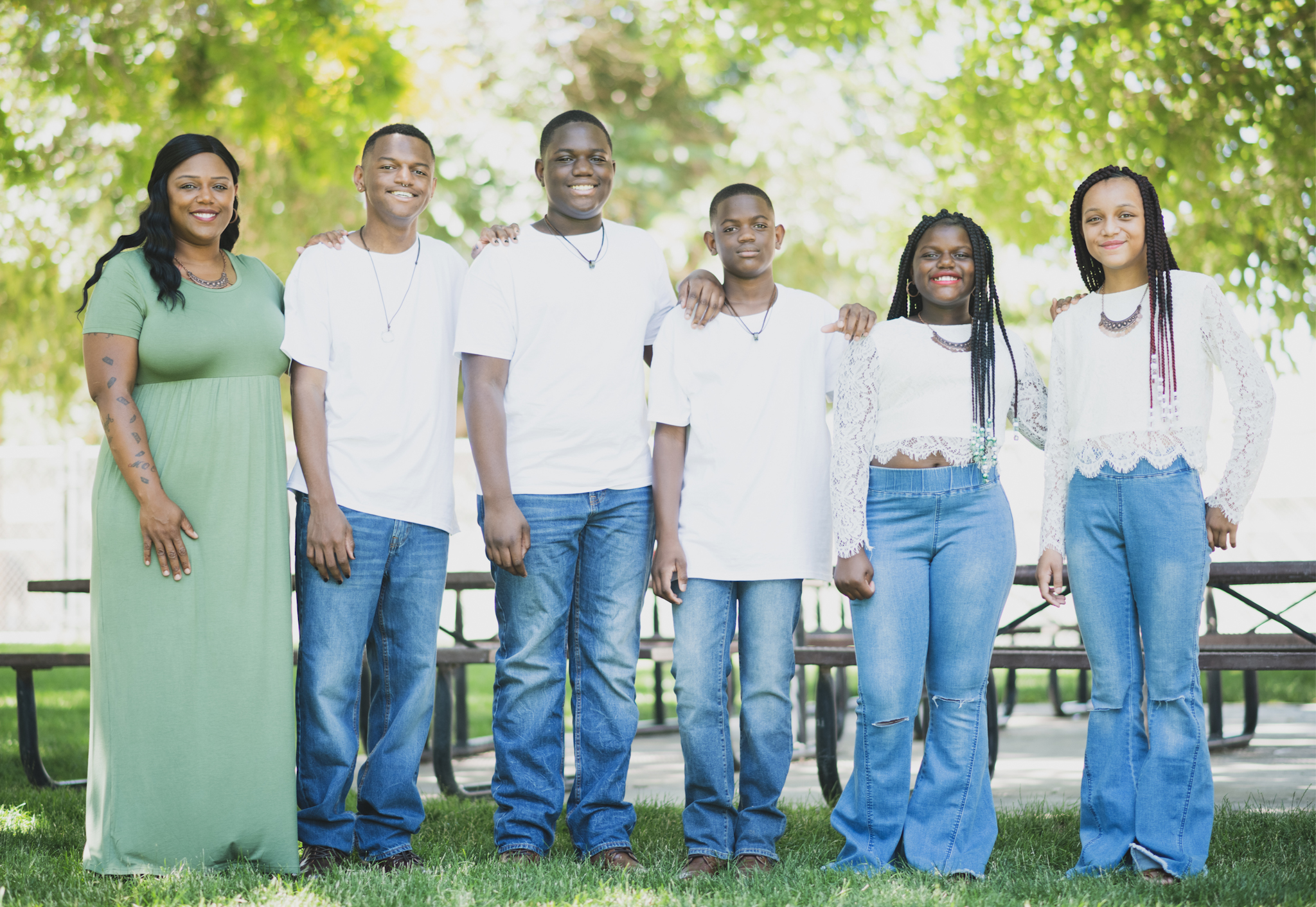 Light and airy family photoshoot at Hesperia Lake Park in the Inland empire. A Large family smiles and laughs for the high deserts best photographer. The scenery is green with lots of beautiful trees and nature. There is a pond in the background of these family portraits in the inland empire