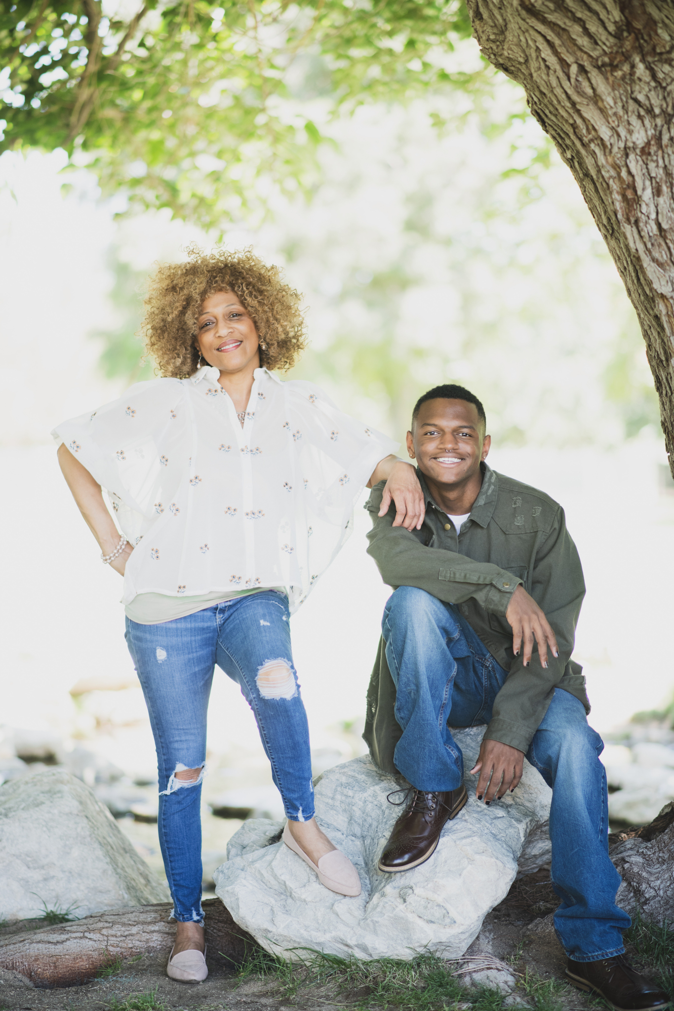 Light and airy family photoshoot at Hesperia Lake Park in the Inland empire. A Large family smiles and laughs for the high deserts best photographer. The scenery is green with lots of beautiful trees and nature. There is a pond in the background of these family portraits in the inland empire