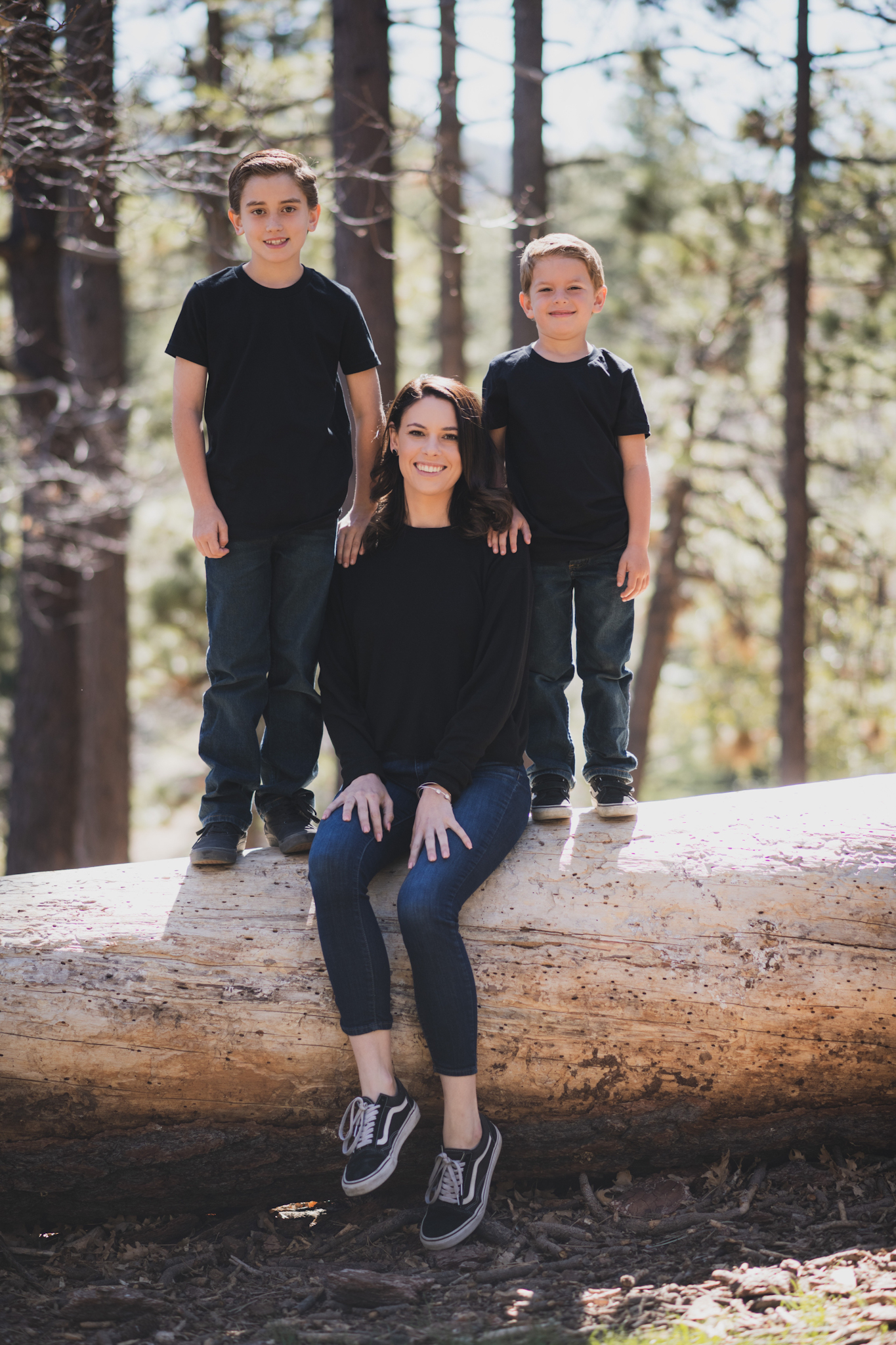 Light and airy portrait of a small family posing for the inland empires best photographer in the green mountains of Wrightwood California. The mother is wearing a white dress with flowers and her two sons are wearing blue shirts and smiling for the camera