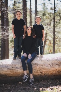 Light and airy portrait of a small family posing for the inland empires best photographer in the green mountains of Wrightwood California. The mother is wearing a white dress with flowers and her two sons are wearing blue shirts and smiling for the camera