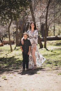 Light and airy portrait of a small family posing for the inland empires best photographer in the green mountains of Wrightwood California. The mother is wearing a white dress with flowers and her two sons are wearing blue shirts and smiling for the camera