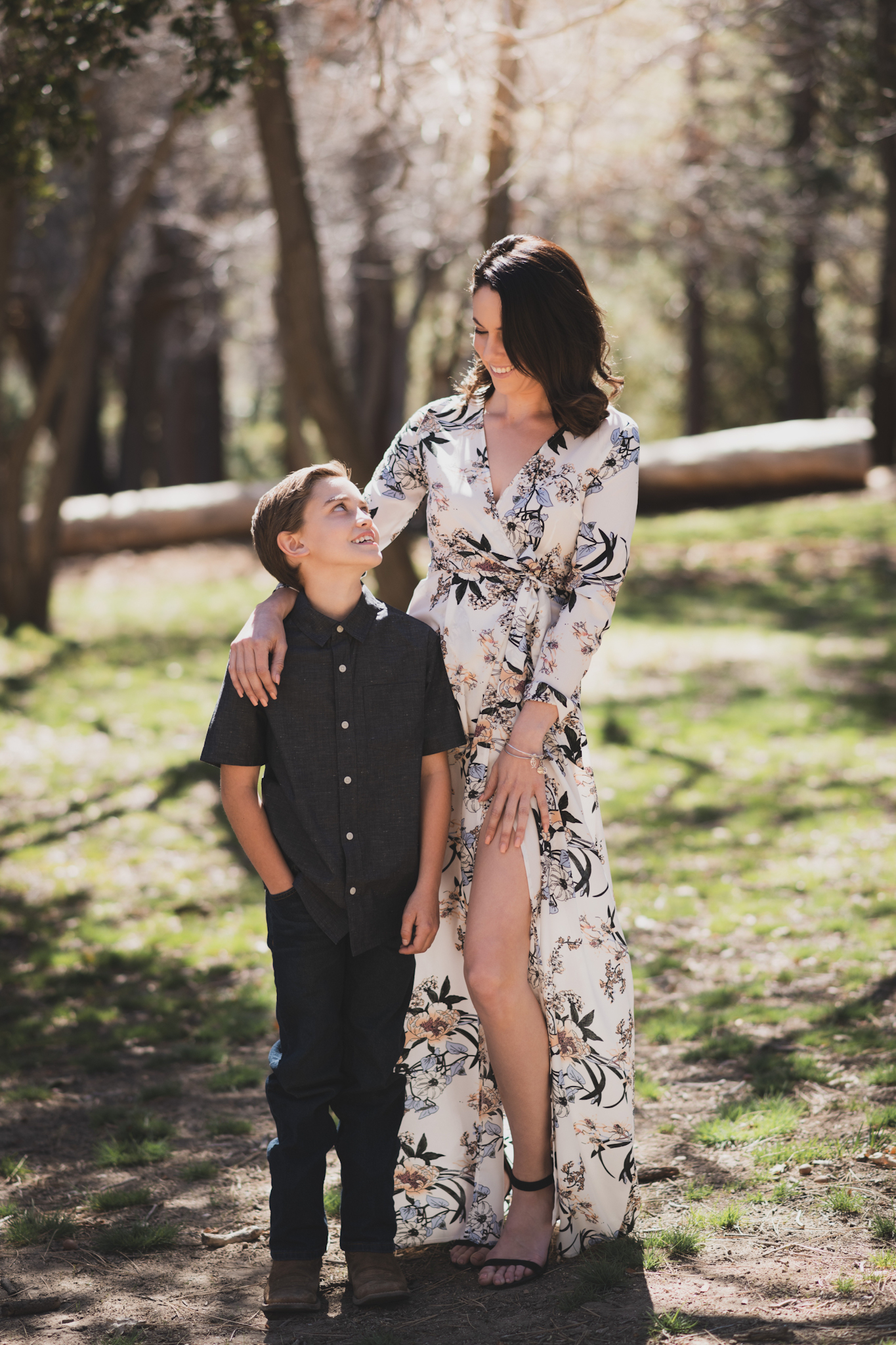 Light and airy portrait of a small family posing for the inland empires best photographer in the green mountains of Wrightwood California. The mother is wearing a white dress with flowers and her two sons are wearing blue shirts and smiling for the camera