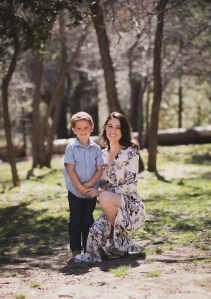 Light and airy portrait of a small family posing for the inland empires best photographer in the green mountains of Wrightwood California. The mother is wearing a white dress with flowers and her two sons are wearing blue shirts and smiling for the camera