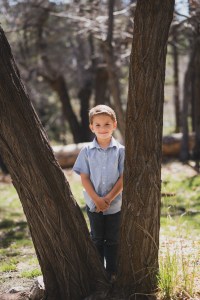 Light and airy portrait of a small family posing for the inland empires best photographer in the green mountains of Wrightwood California. The mother is wearing a white dress with flowers and her two sons are wearing blue shirts and smiling for the camera