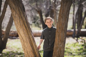 Light and airy portrait of a small family posing for the inland empires best photographer in the green mountains of Wrightwood California. The mother is wearing a white dress with flowers and her two sons are wearing blue shirts and smiling for the camera
