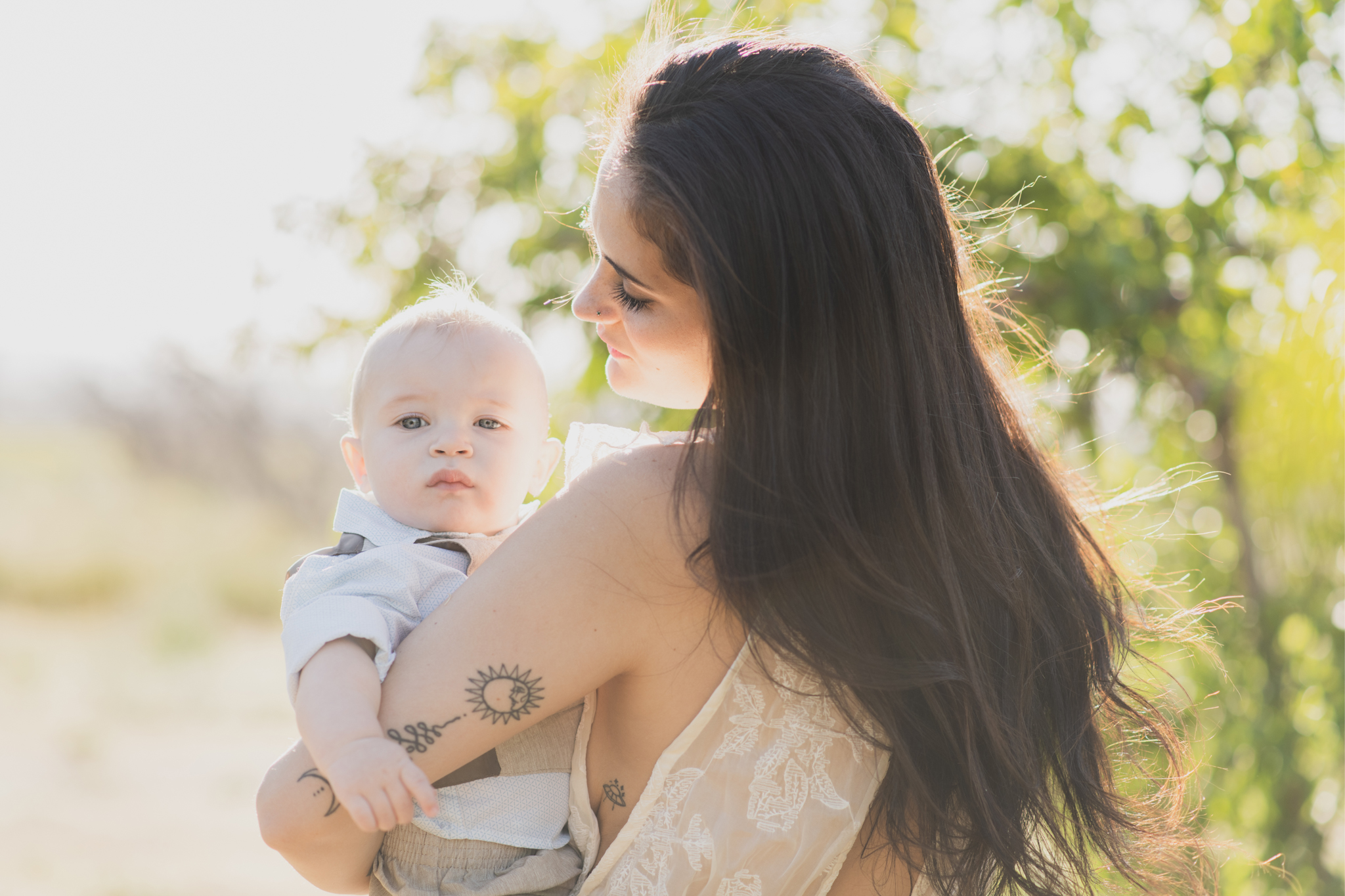 Light and airy portrait of a family in a peach orchard in the high desert. They are smiling for the high deserts best family photographer. the mother is wearing a white dress around green trees. The father and son both are wearing blue shirts and grey vests. The four year old daughter dances and spins for the camera in the inland empire