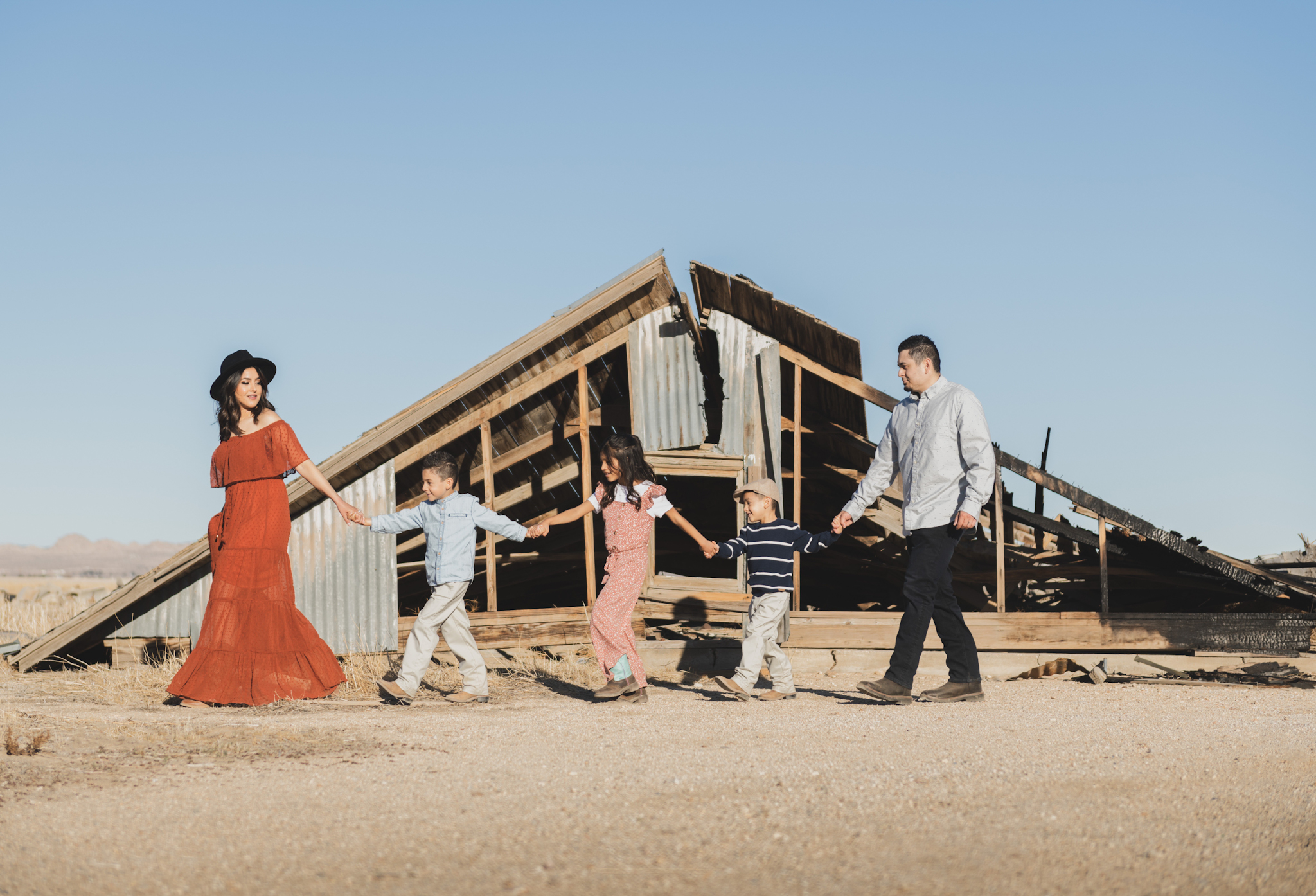 Light and airy portraits of a family in Lucerne Valley California in the High Desert. Three small children are laughing and playing. The desert background is warm with lots of sun, joshua trees and mountains. The mother is wearing a red dress in these inland empire pictures