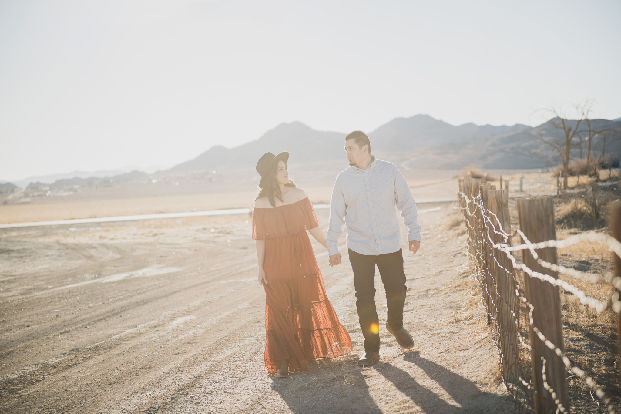 Light and airy portraits of a family in Lucerne Valley California in the High Desert. Three small children are laughing and playing. The desert background is warm with lots of sun, joshua trees and mountains. The mother is wearing a red dress in these inland empire pictures