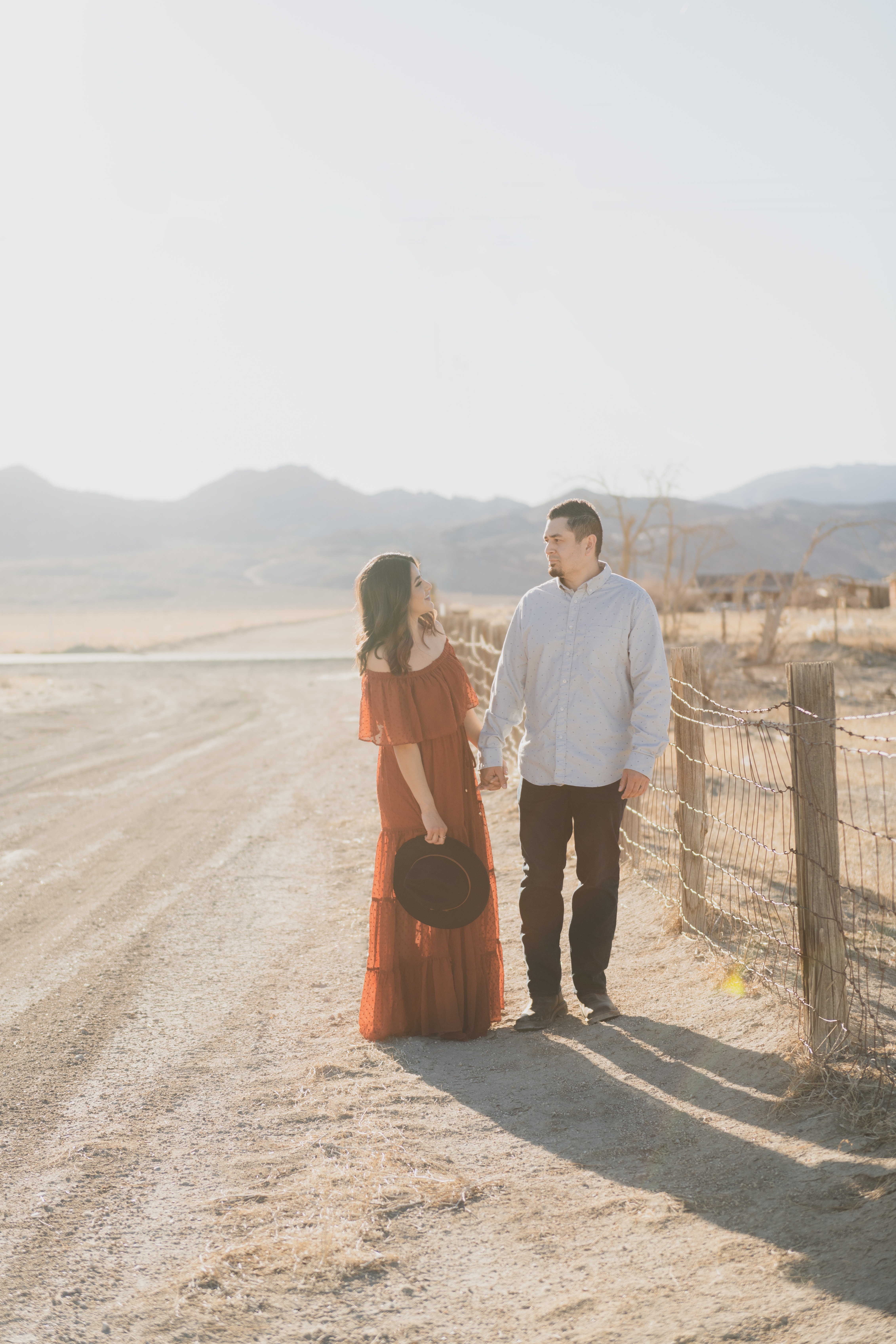 Light and airy portraits of a family in Lucerne Valley California in the High Desert. Three small children are laughing and playing. The desert background is warm with lots of sun, joshua trees and mountains. The mother is wearing a red dress in these inland empire pictures