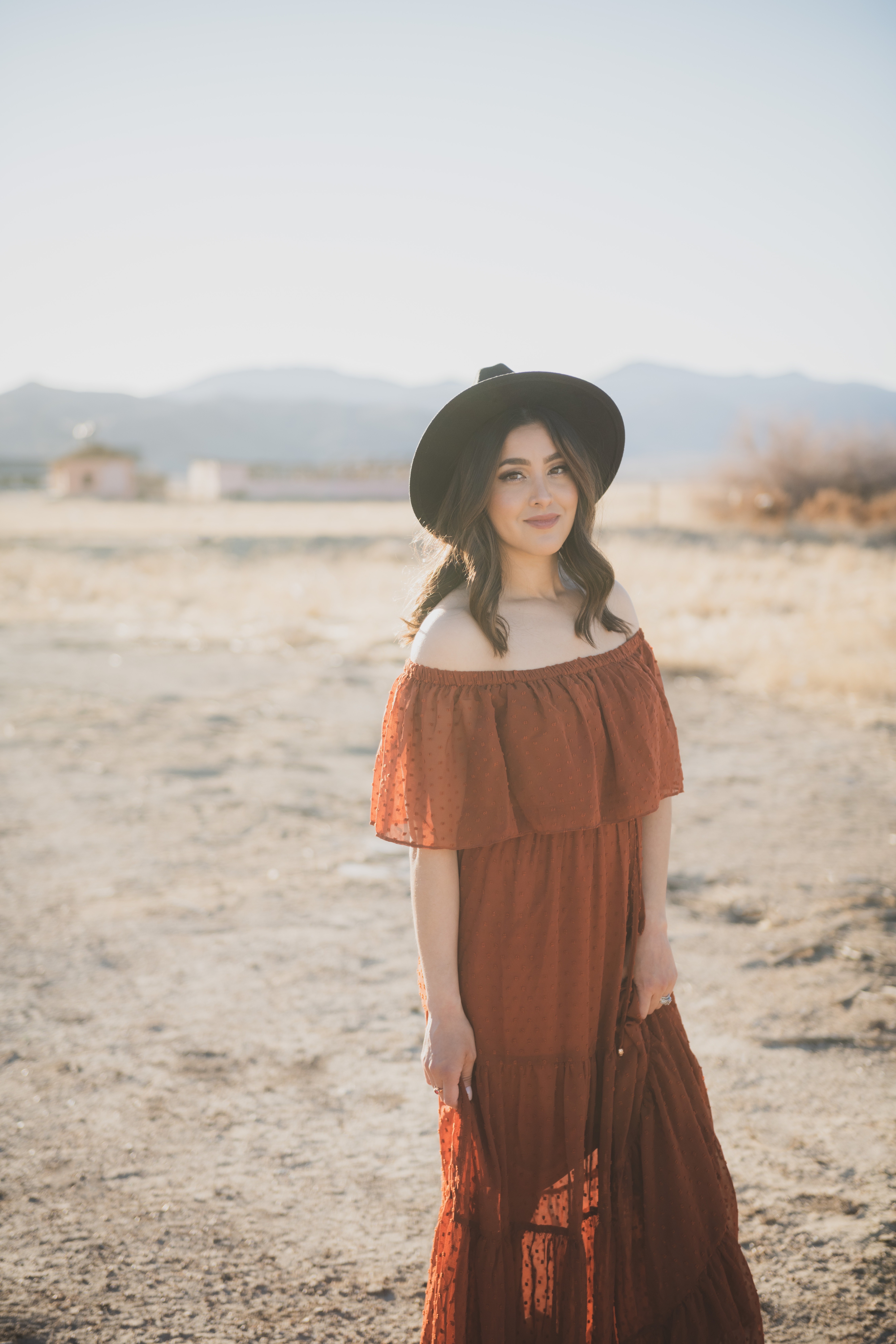 Light and airy portraits of a family in Lucerne Valley California in the High Desert. Three small children are laughing and playing. The desert background is warm with lots of sun, joshua trees and mountains. The mother is wearing a red dress in these inland empire pictures