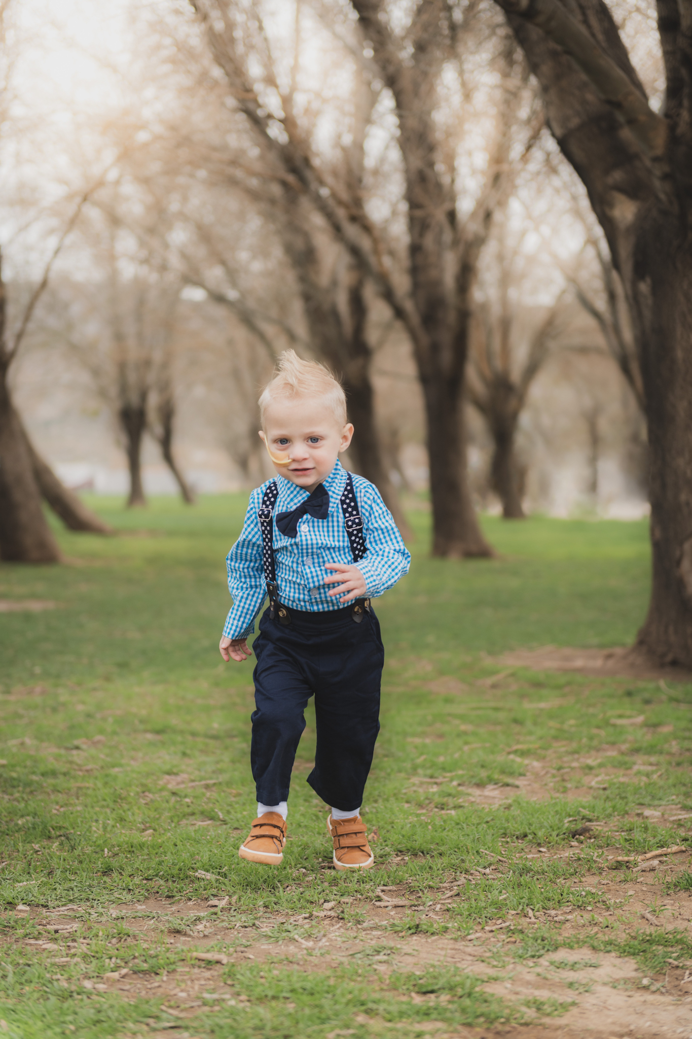 Light and air pictures of a three year old blonde boy playing in the grass at Hesperia Lakes park in Hesperia California in the High desert mountains. Little boy is playing with bubbles and laughing while wearing a blue bow tie and suspenders and playing with ducks