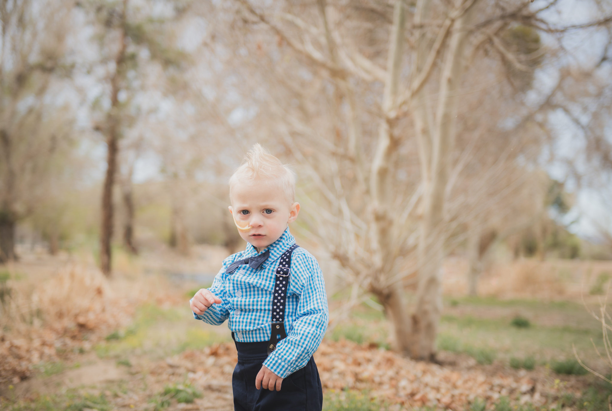 Light and air pictures of a three year old blonde boy playing in the grass at Hesperia Lakes park in Hesperia California in the High desert mountains. Little boy is playing with bubbles and laughing while wearing a blue bow tie and suspenders