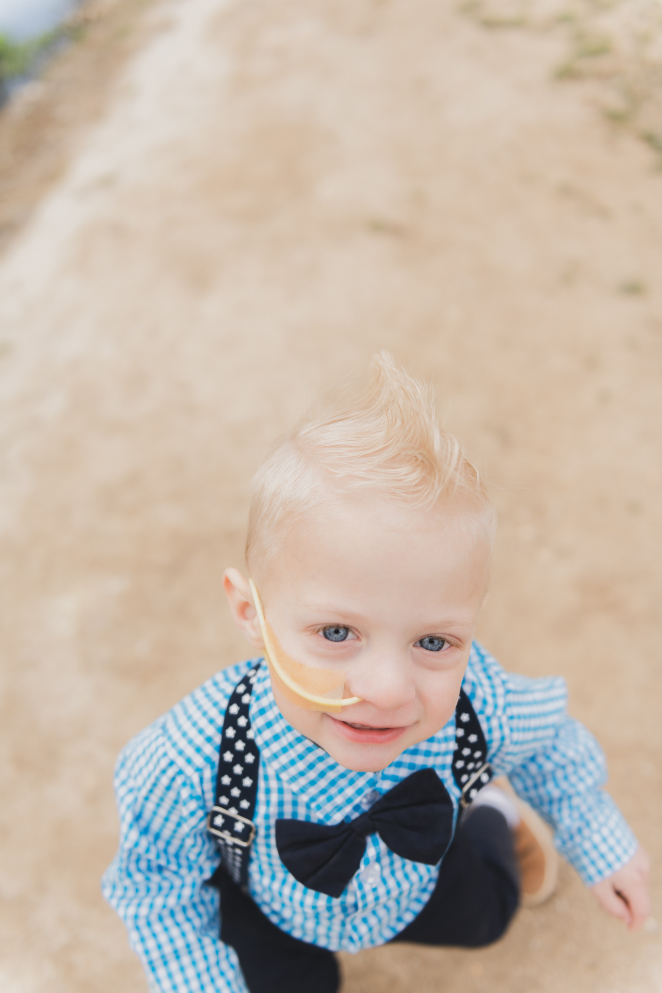 Light and air pictures of a three year old blonde boy playing in the grass at Hesperia Lakes park in Hesperia California in the High desert mountains. Little boy is playing with bubbles and laughing while wearing a blue bow tie and suspenders