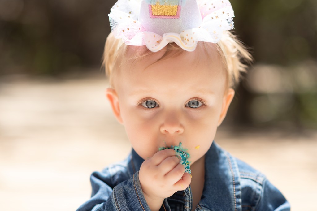Light and airy pictures of a baby girl sitting on a magical bridge in the mountains of Wrightwood California. Baby is smashing a colorful cake and smearing it on her face in these high desert portraits