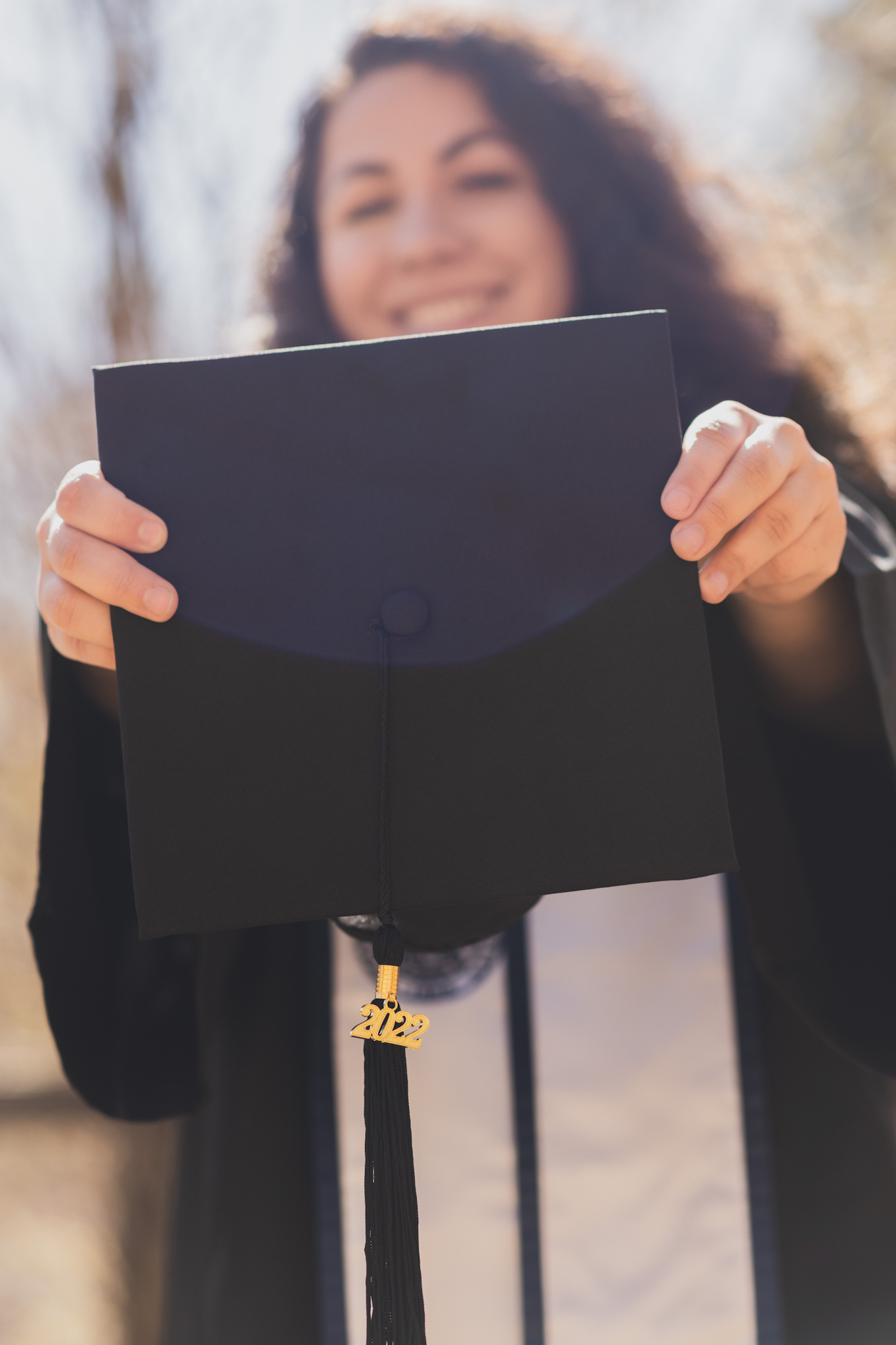 Light and airy portraits of a young woman in a graduation cap and gown. Woman is smiling and happy in the Wrightwood mountains of california. She is happy and throwing her cap in the air surrounded by large trees in these high desert pictures
