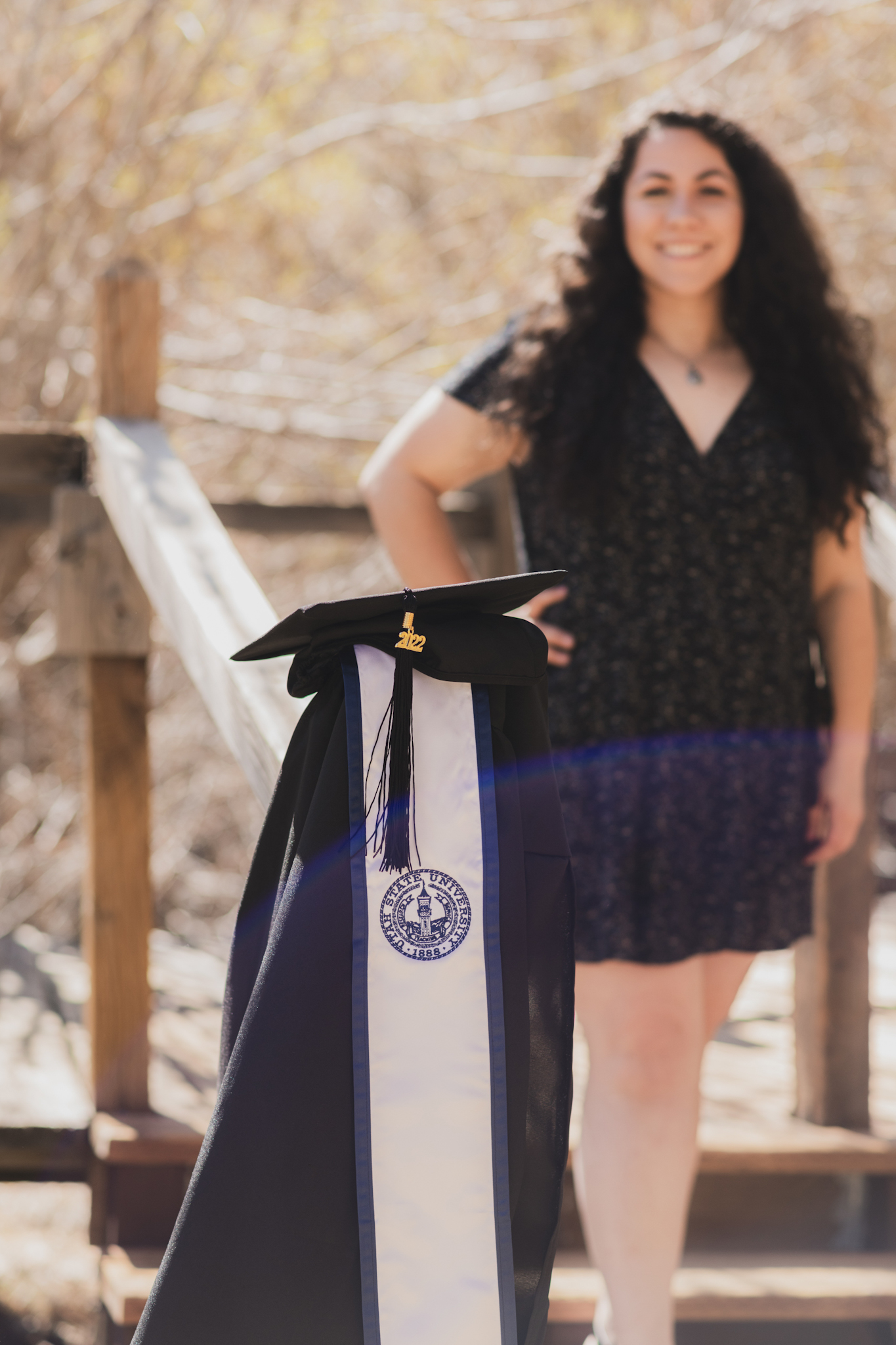 Light and airy portraits of a young woman in a graduation cap and gown. Woman is smiling and happy in the Wrightwood mountains of california. She is happy and throwing her cap in the air surrounded by large trees in these high desert pictures