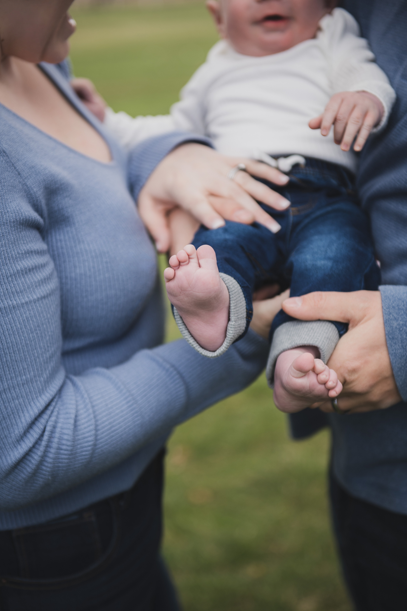 Light and airy pictures of a couple with a baby boy. Couple is wearing blue holding baby boy and smiling in these high desert portraits shot in the beautiful Hesperia Lakes park in the inland empire. There is a tree with white flowers blooming in the background