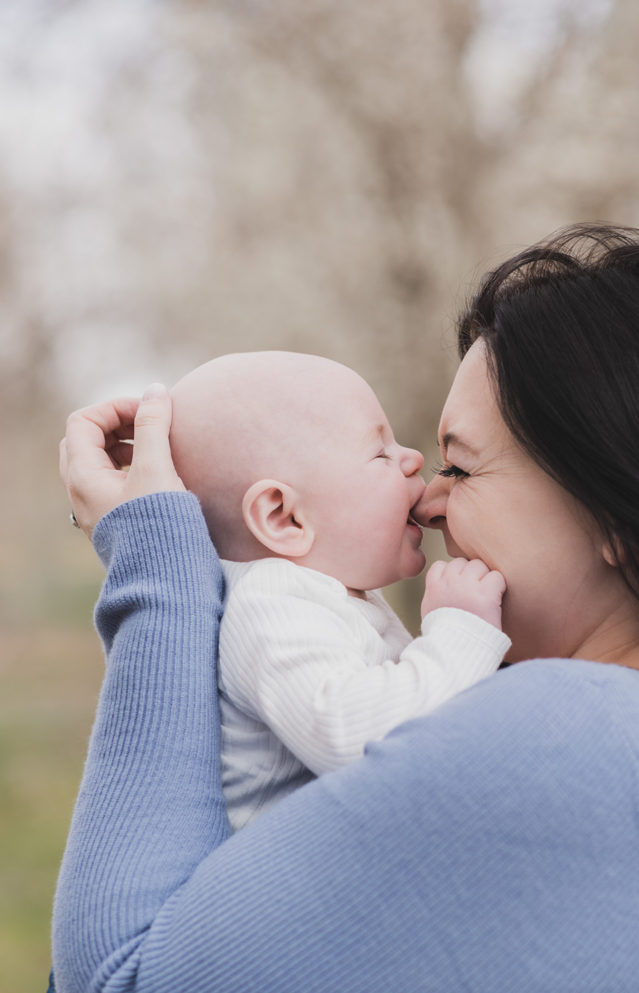 Light and airy pictures of a couple with a baby boy. Couple is wearing blue holding baby boy and smiling in these high desert portraits shot in the beautiful Hesperia Lakes park in the inland empire. There is a tree with white flowers blooming in the background