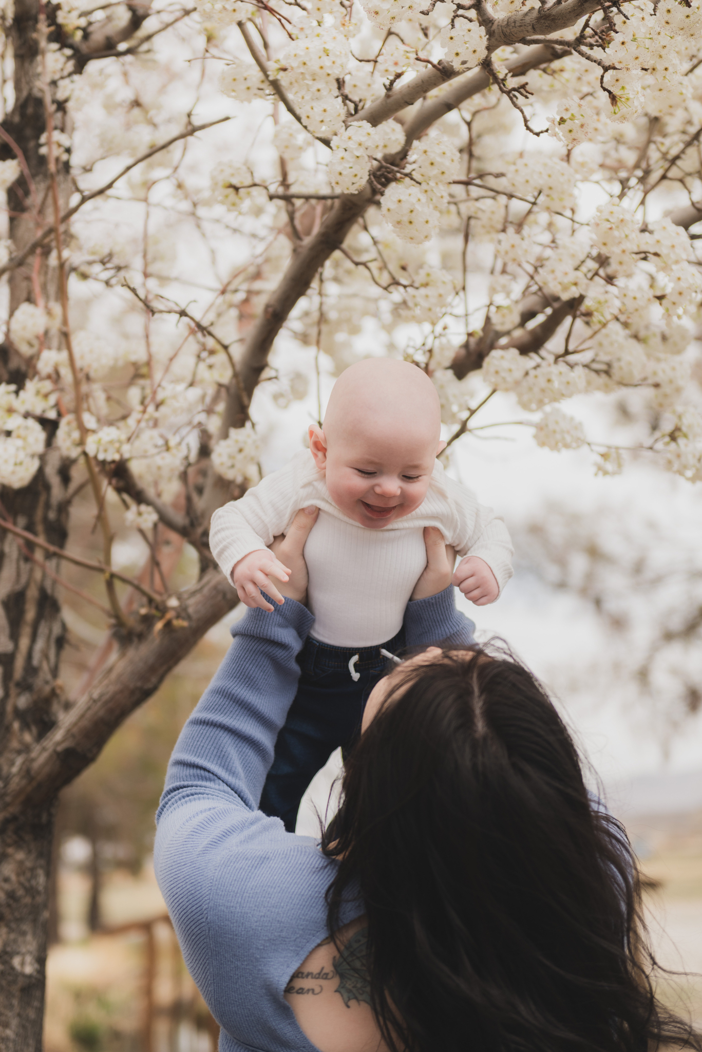 Light and airy pictures of a couple with a baby boy. Couple is wearing blue holding baby boy and smiling in these high desert portraits shot in the beautiful Hesperia Lakes park in the inland empire. There is a tree with white flowers blooming in the background