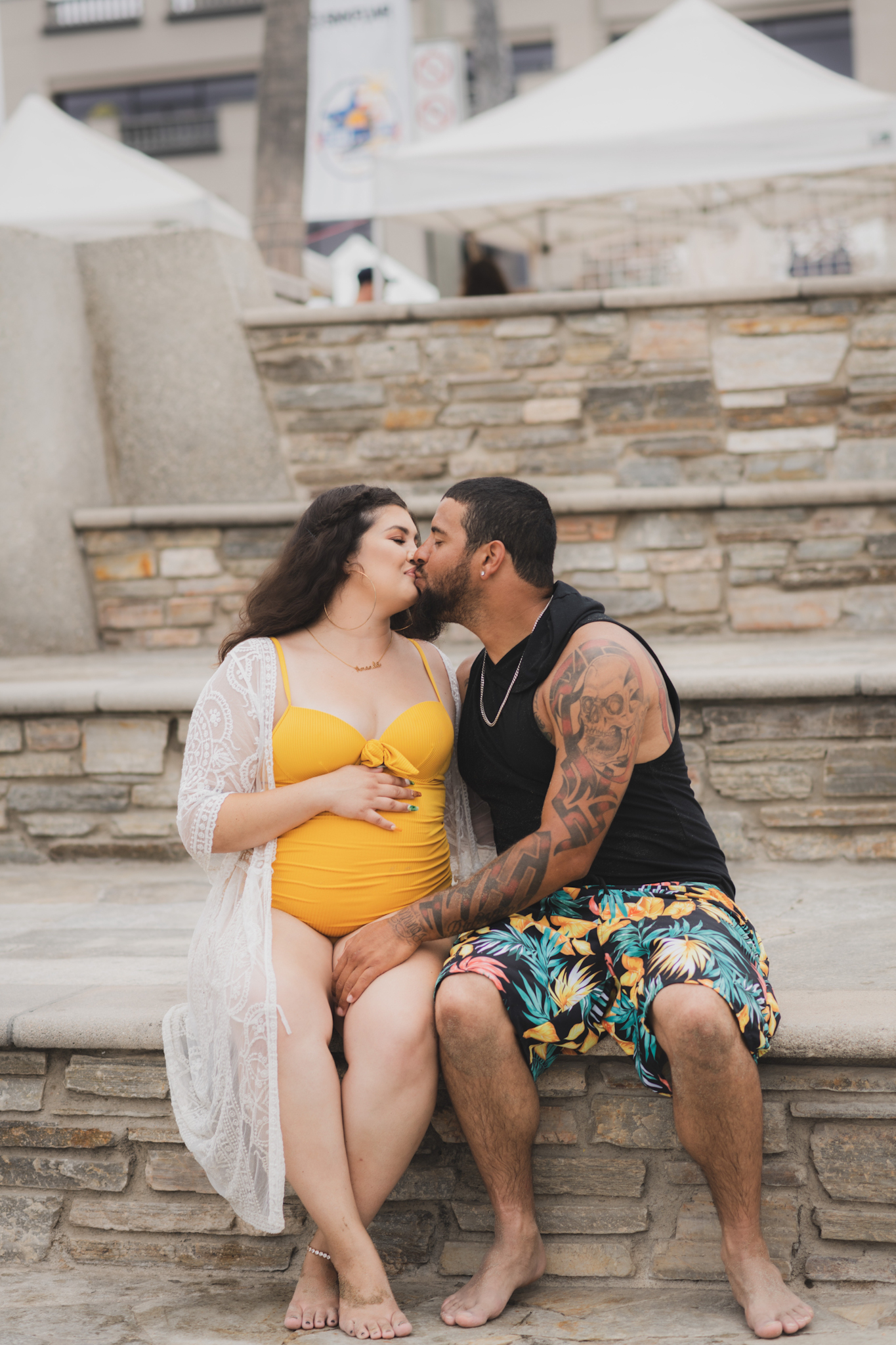 Light and airy portraits of a maternity shoot with family. Pregnant mother is wearing a bright yellow bathing suite in these Huntington Beach pictures. You can see blue waves in the background, the pier and husband and baby boy smiling with mother. Inland empire photoshoot at the beach