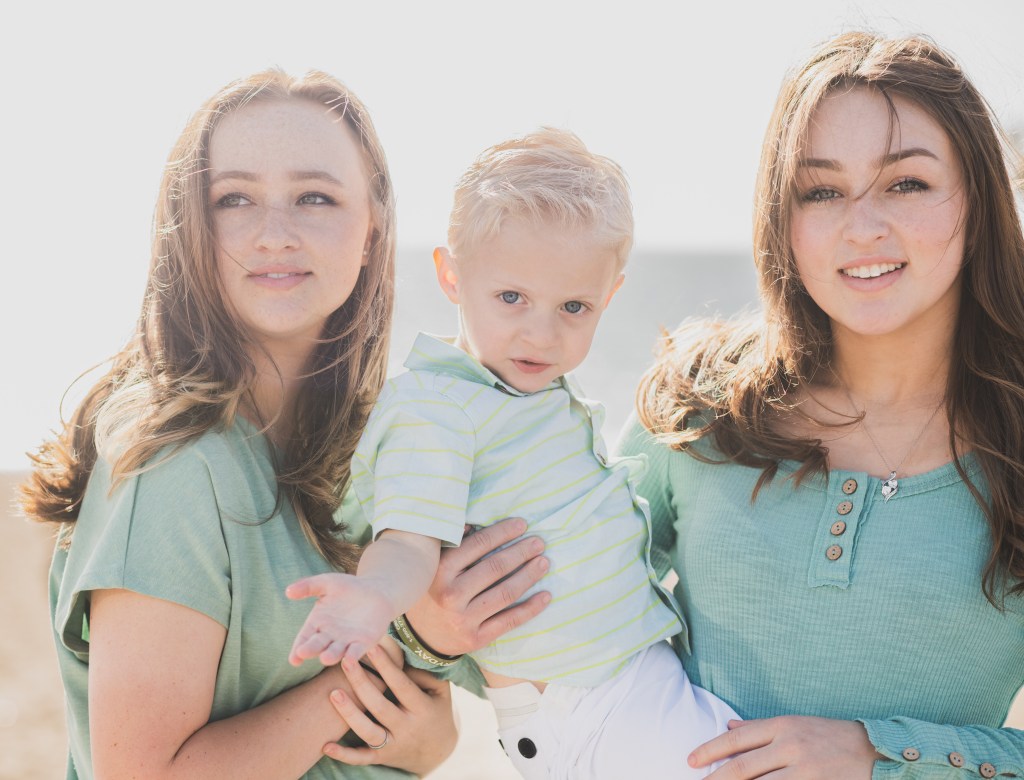 Light and airy shoot of a family at the beach. A little blonde boy named Bradley got adopted and they are celebrating. He now has two older sisters who hold his hands in the water and a beautiful mother with dark hair that plays with him in the waves. He is loved