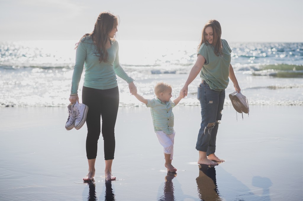 Light and airy shoot of a family at the beach. A little blonde boy named Bradley got adopted and they are celebrating. He now has two older sisters who hold his hands in the water and a beautiful mother with dark hair that plays with him in the waves. He is loved