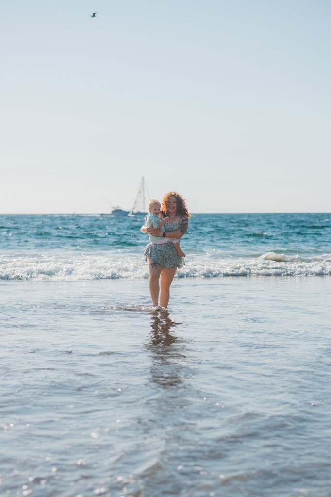 Light and airy shoot of a family at the beach. A little blonde boy named Bradley got adopted and they are celebrating. He now has two older sisters who hold his hands in the water and a beautiful mother with dark hair that plays with him in the waves. He is loved