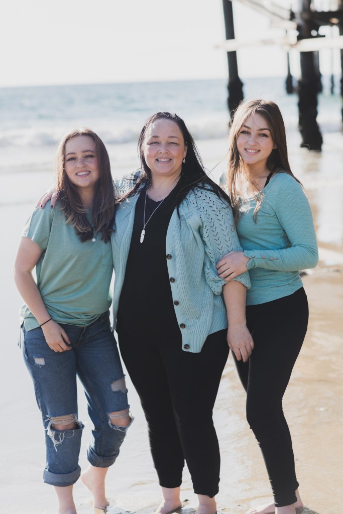 Light and airy shoot of a family at the beach. A little blonde boy named Bradley got adopted and they are celebrating. He now has two older sisters who hold his hands in the water and a beautiful mother with dark hair that plays with him in the waves. He is loved