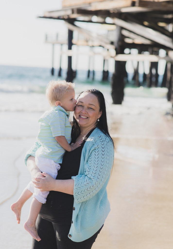 Light and airy shoot of a family at the beach. A little blonde boy named Bradley got adopted and they are celebrating. He now has two older sisters who hold his hands in the water and a beautiful mother with dark hair that plays with him in the waves. He is loved